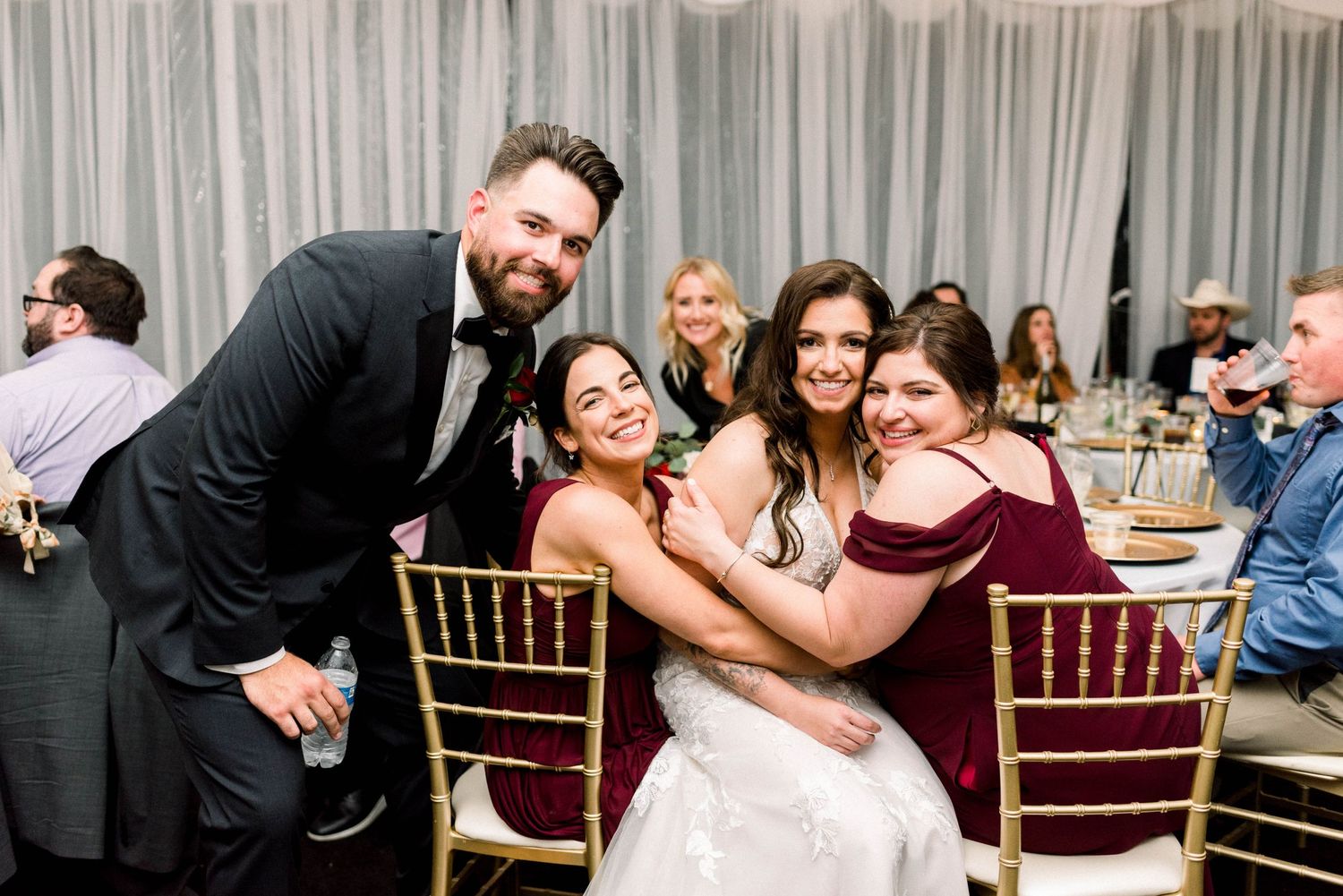 Wedding party posing and laughing together at reception tables with festive decorations.