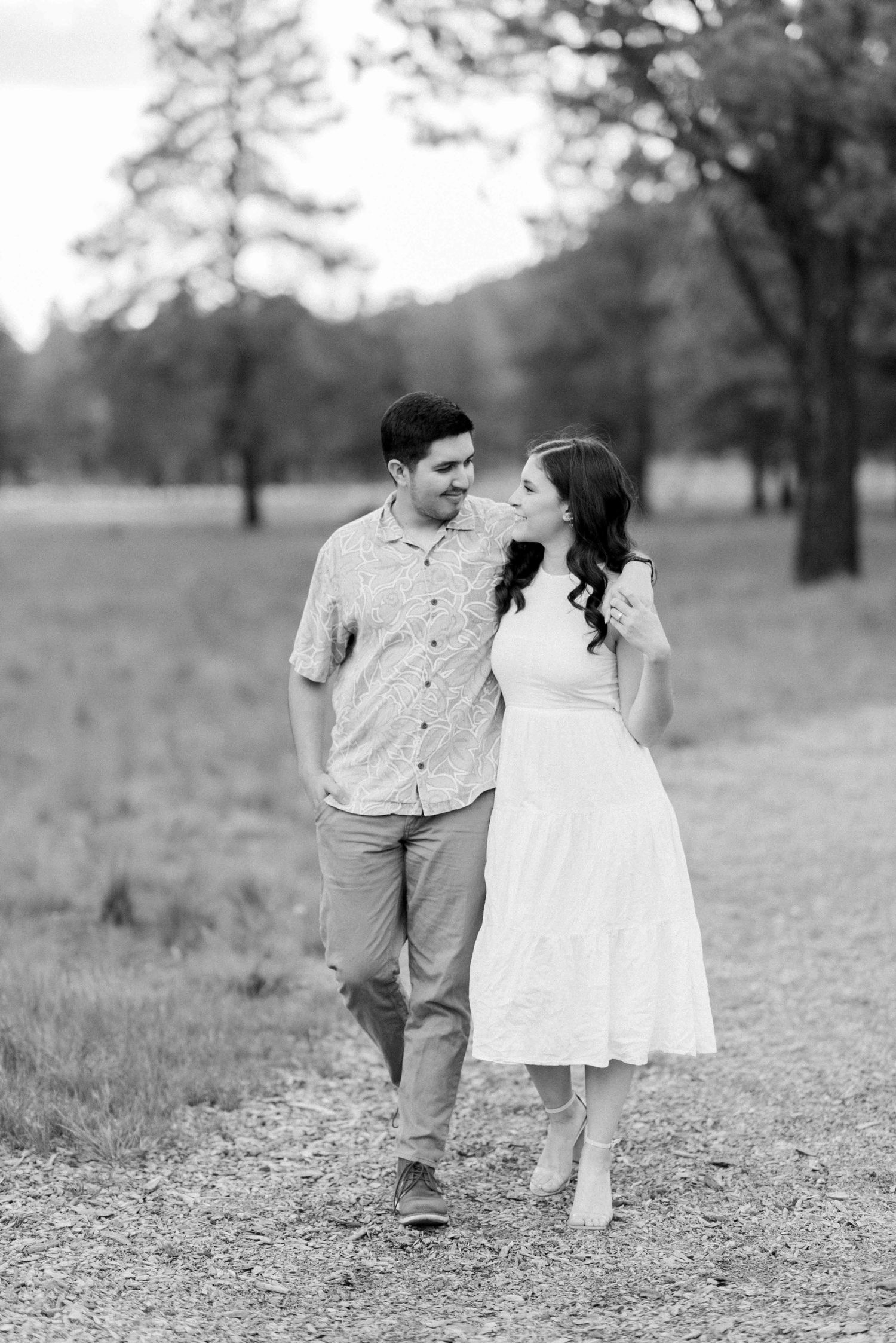 A couple takes a romantic stroll along a path through a wooded area in black and white.