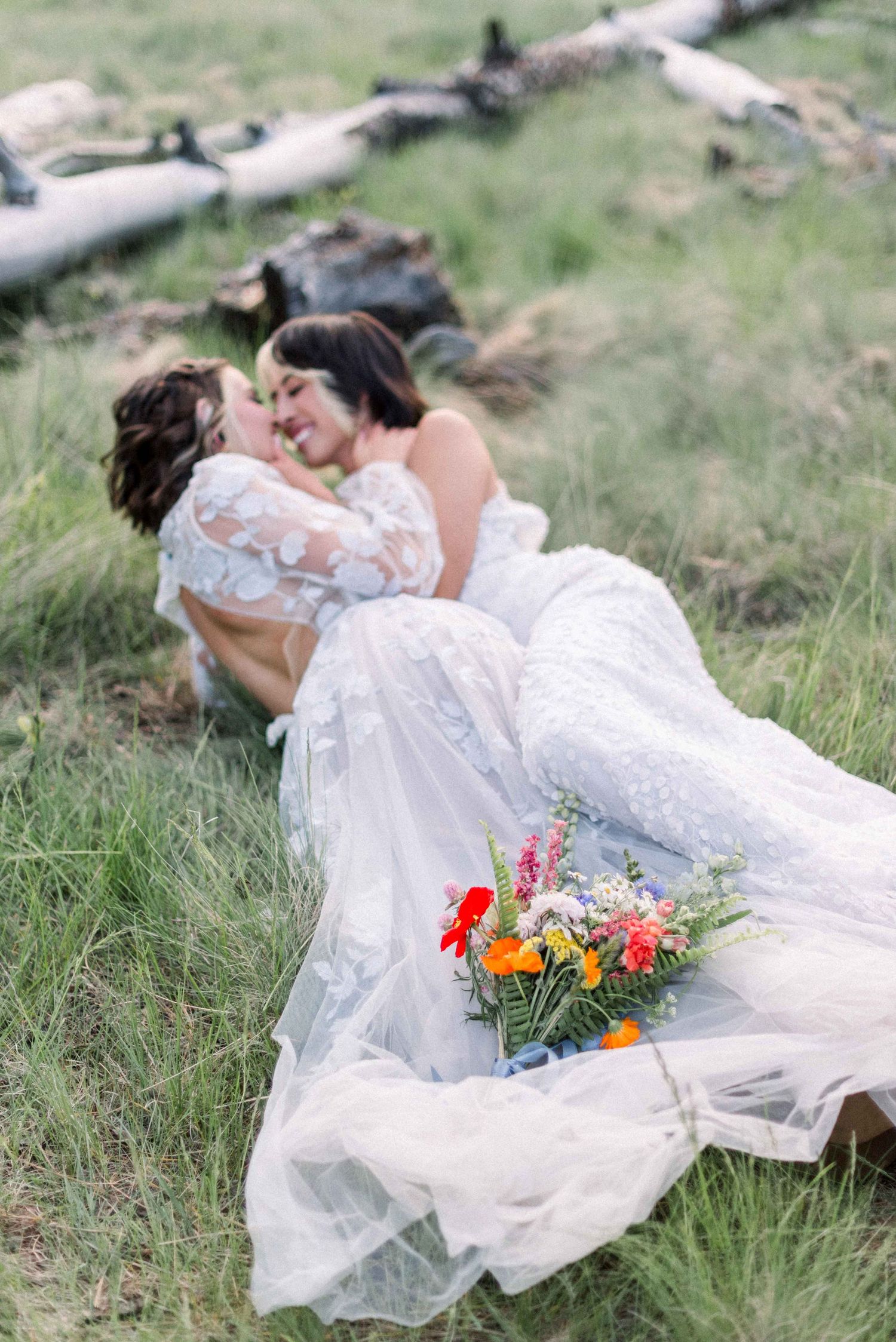 A romantic wedding couple lounging in grass with colorful wildflower bouquet nearby.