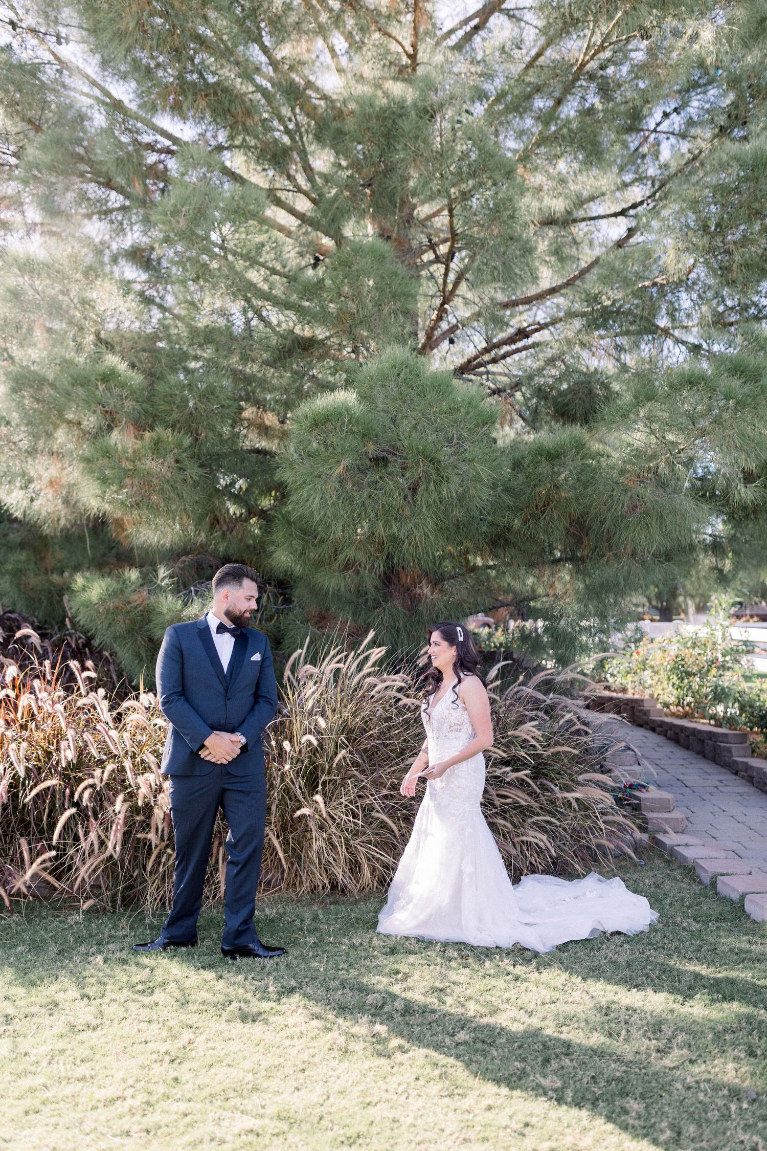 A couple's first look wedding moment in a garden setting with tall pine trees and ornamental grasses.