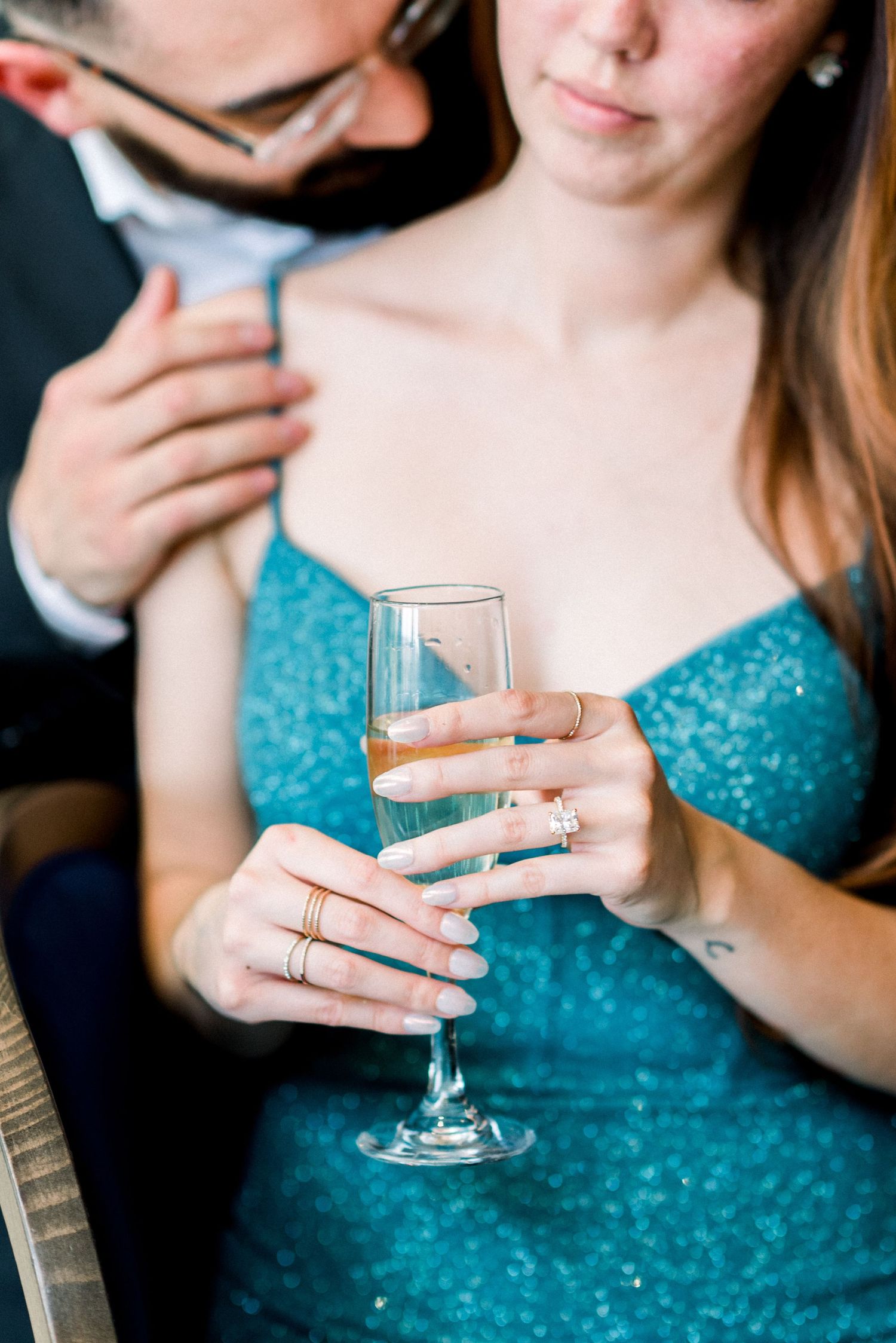 Close up of hands holding champagne flute showing sparkling dress details and jewelry.
