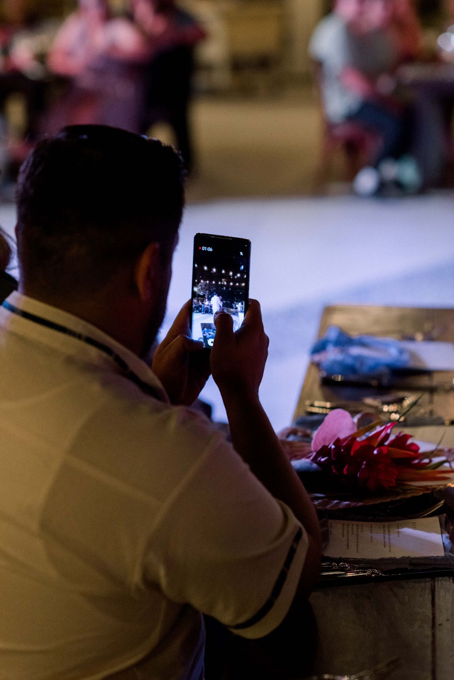 A guest in white captures photos on their phone during a wedding reception.