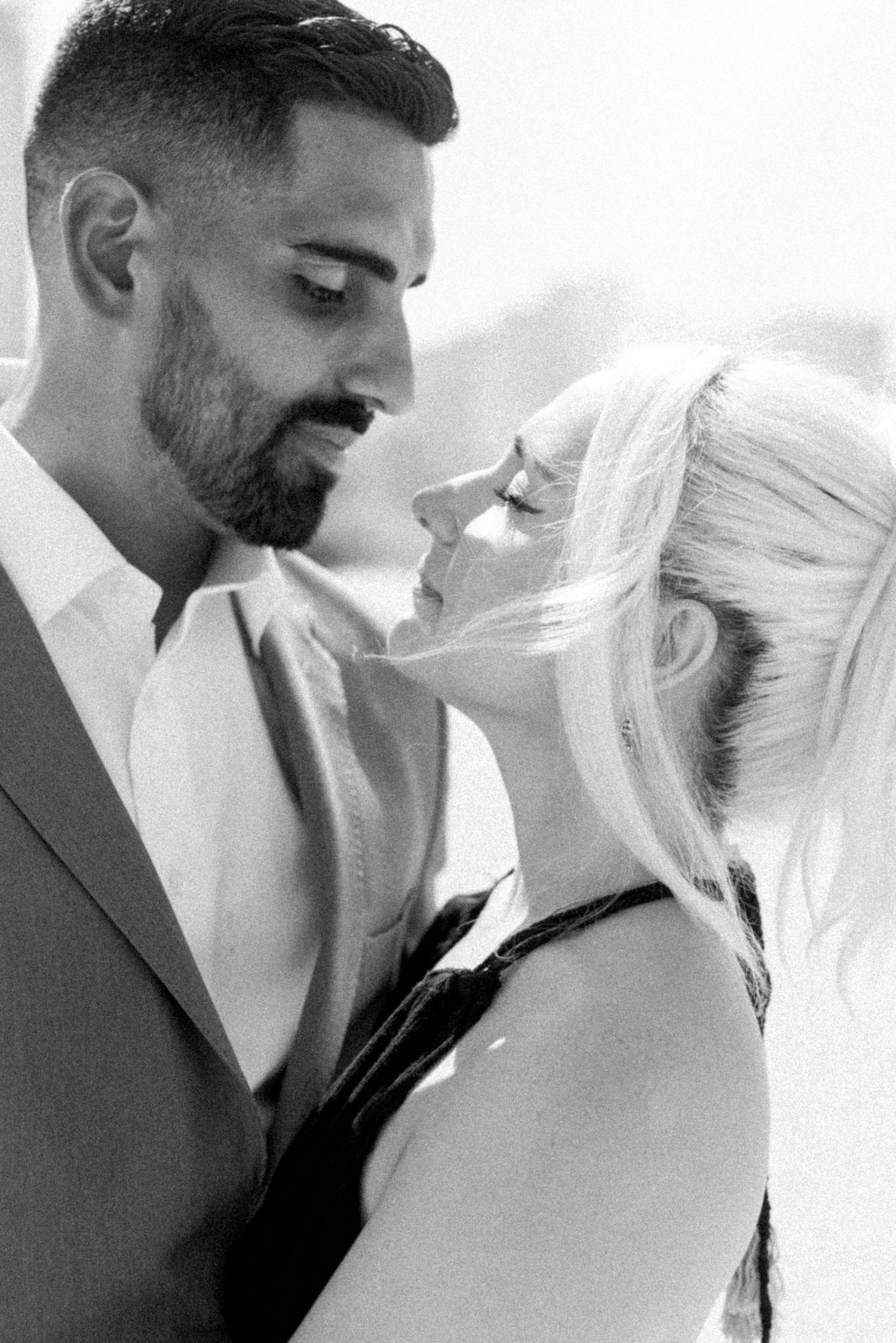 Intimate black and white portrait of couple sharing romantic moment in formal attire.