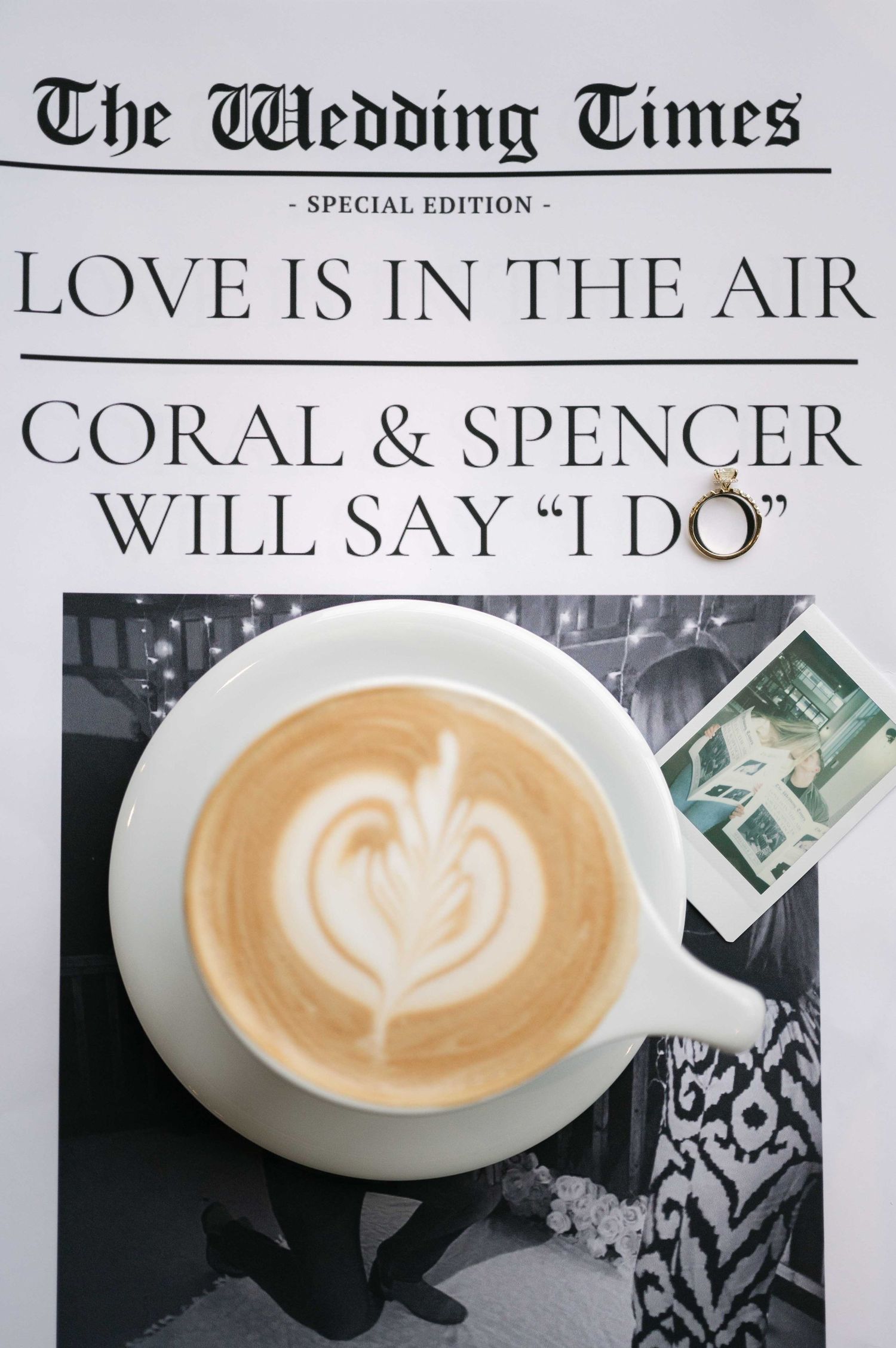 A coffee cup with latte art sits on a custom wedding newspaper announcement.