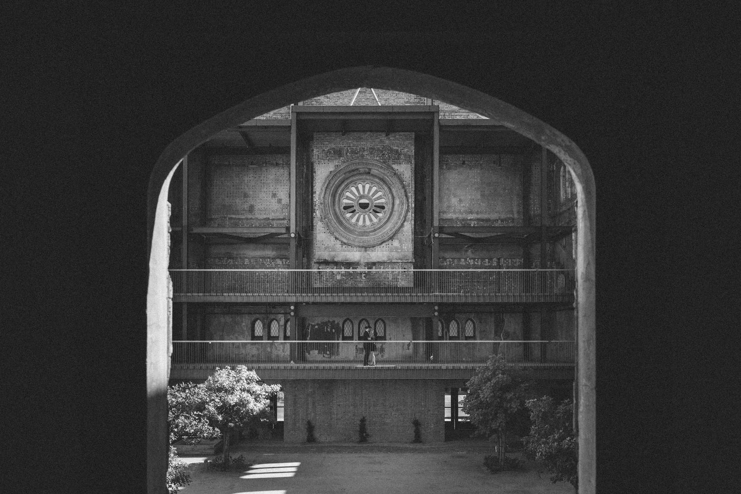 Black and white view through archway of circular window and shelving in historic interior space.
