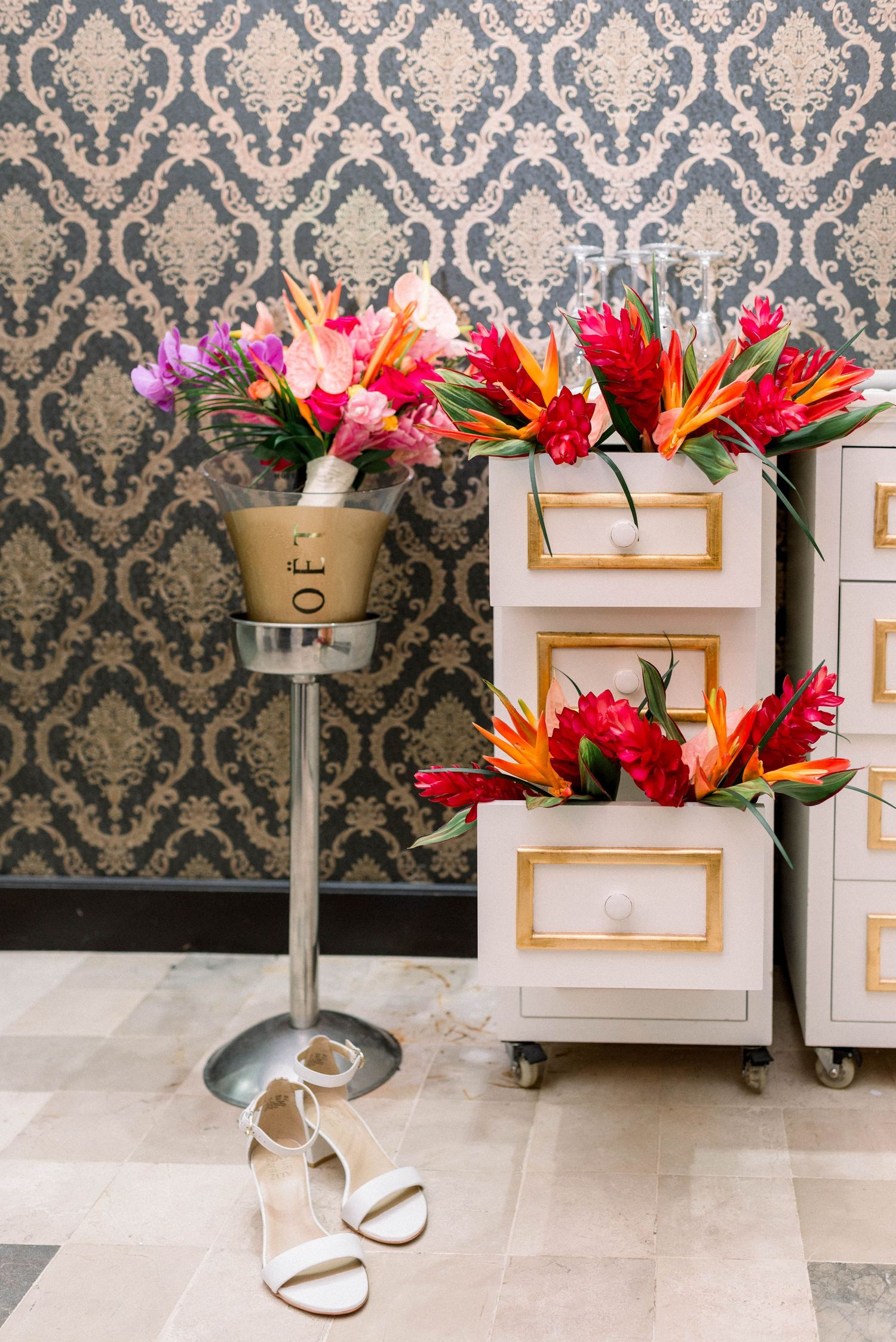Tropical floral arrangements with birds of paradise and roses against damask wallpaper.