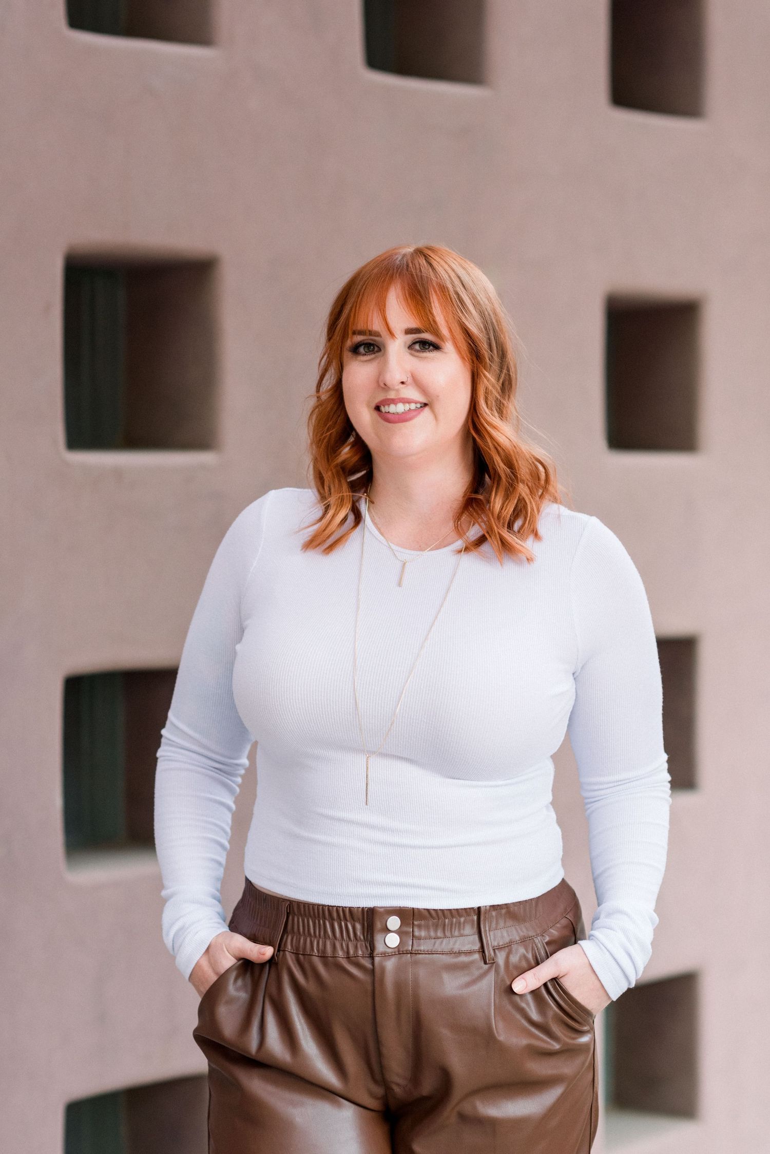 Stylish outfit featuring white fitted top and brown leather pants against modern architectural background.