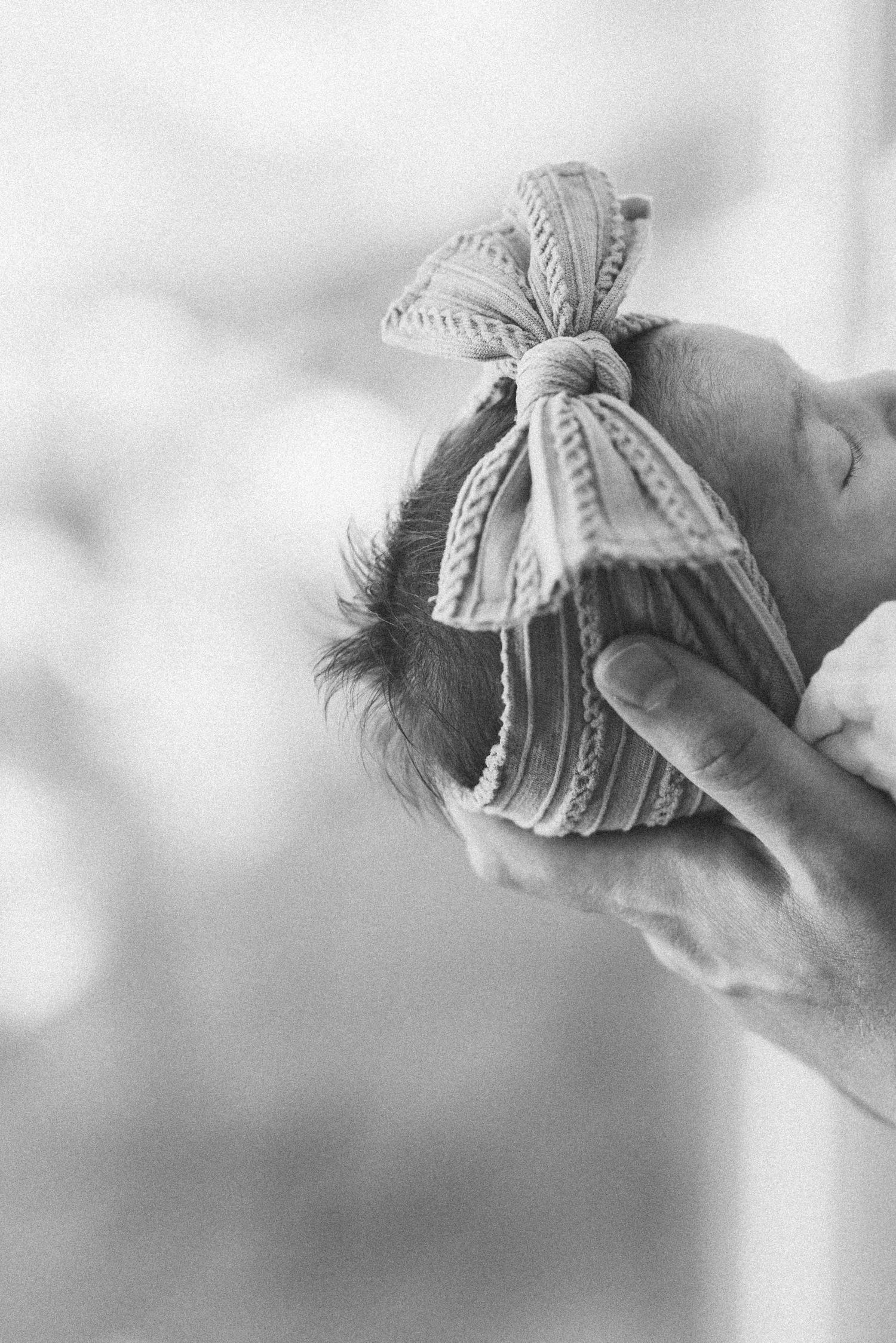 Black and white photo of newborn wearing decorative bow headband.