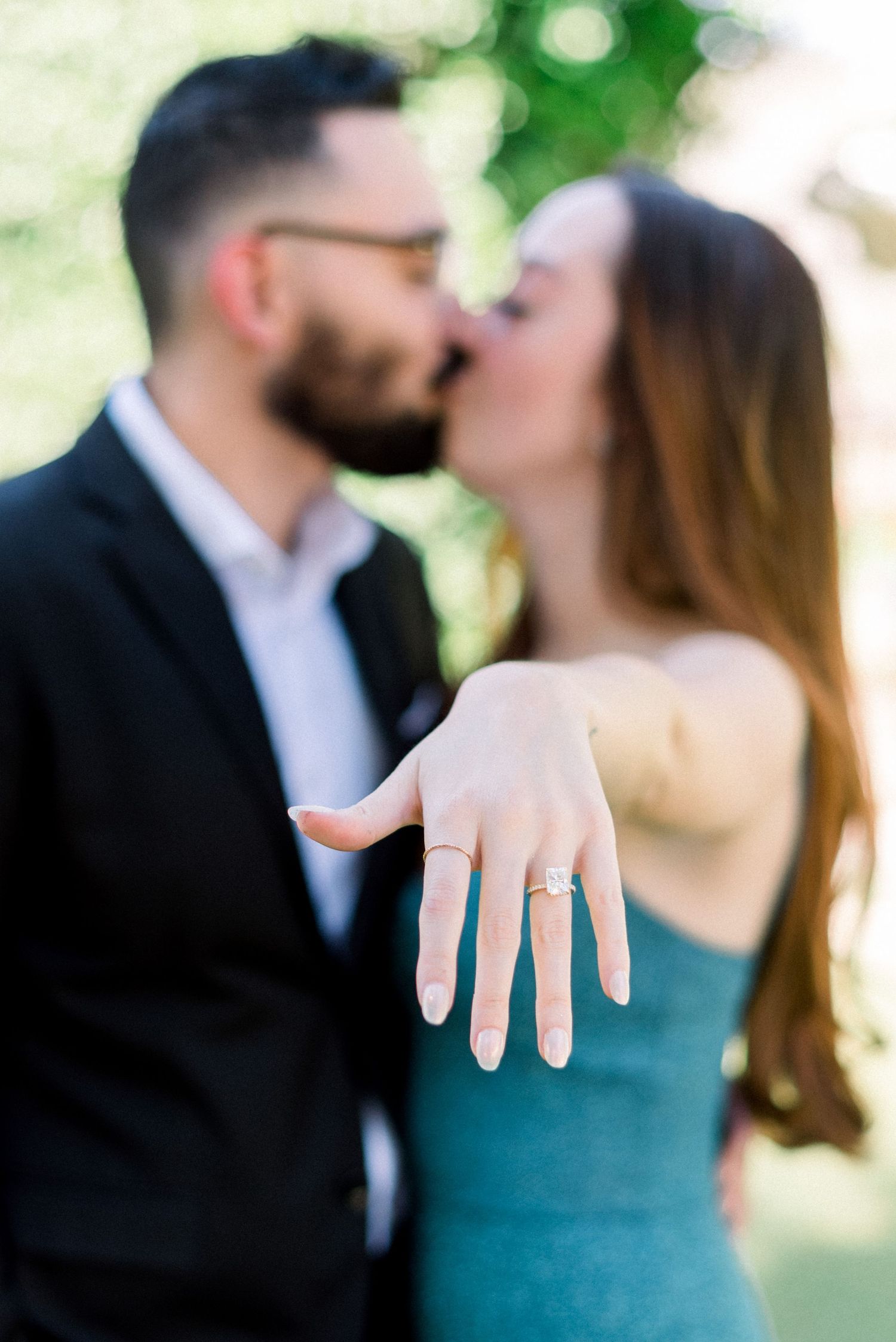 A romantic kiss while displaying the engagement ring in a garden setting.
