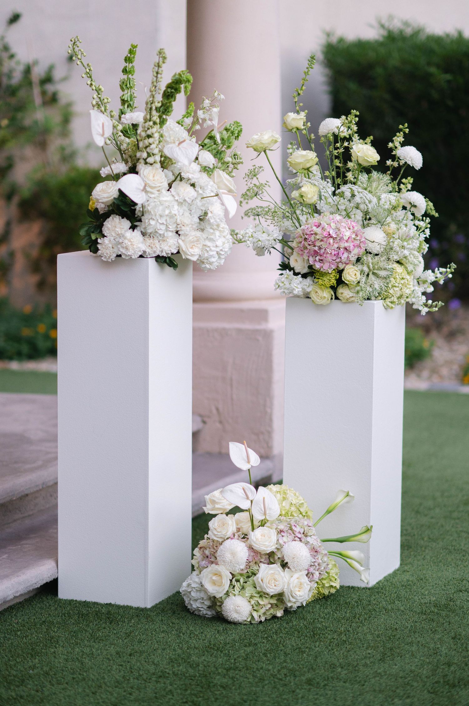 White floral arrangements in modern square pedestals on grass at outdoor wedding.