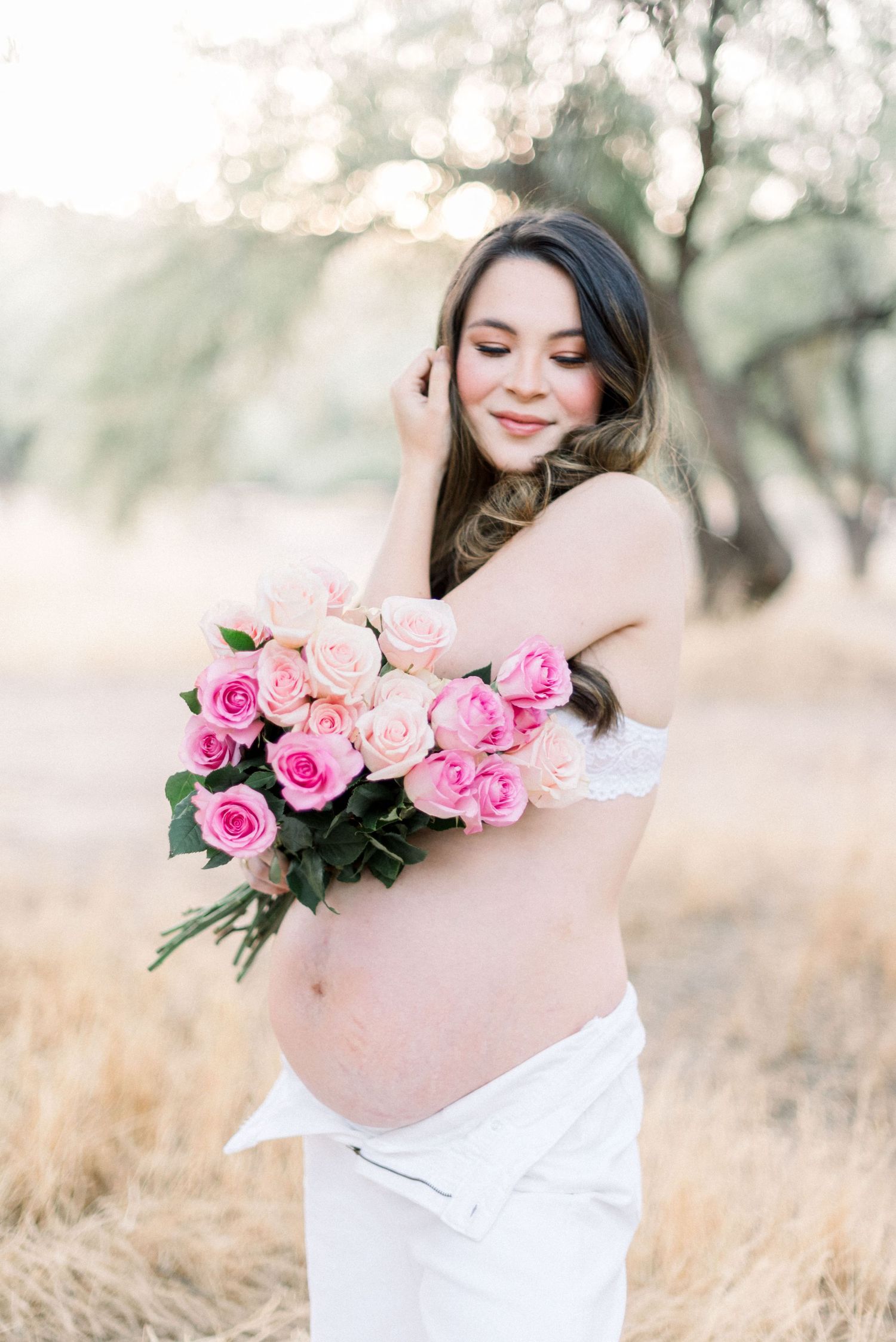 Dreamy outdoor maternity photo series featuring a white dress and pink roses against a soft natural background.