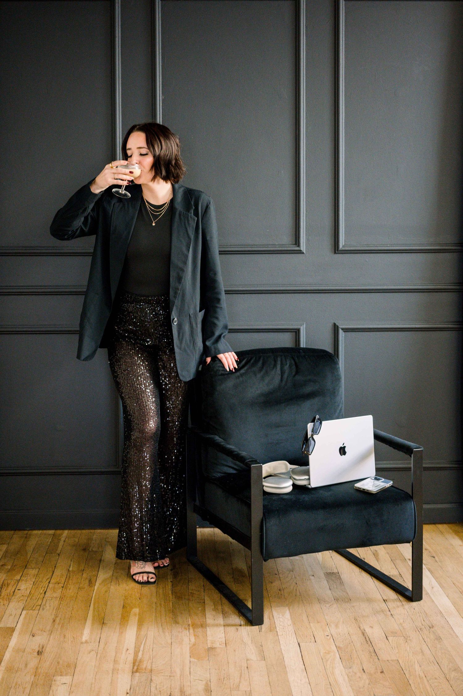A stylish portrait of someone in a sequined outfit and blazer against a dark paneled wall.