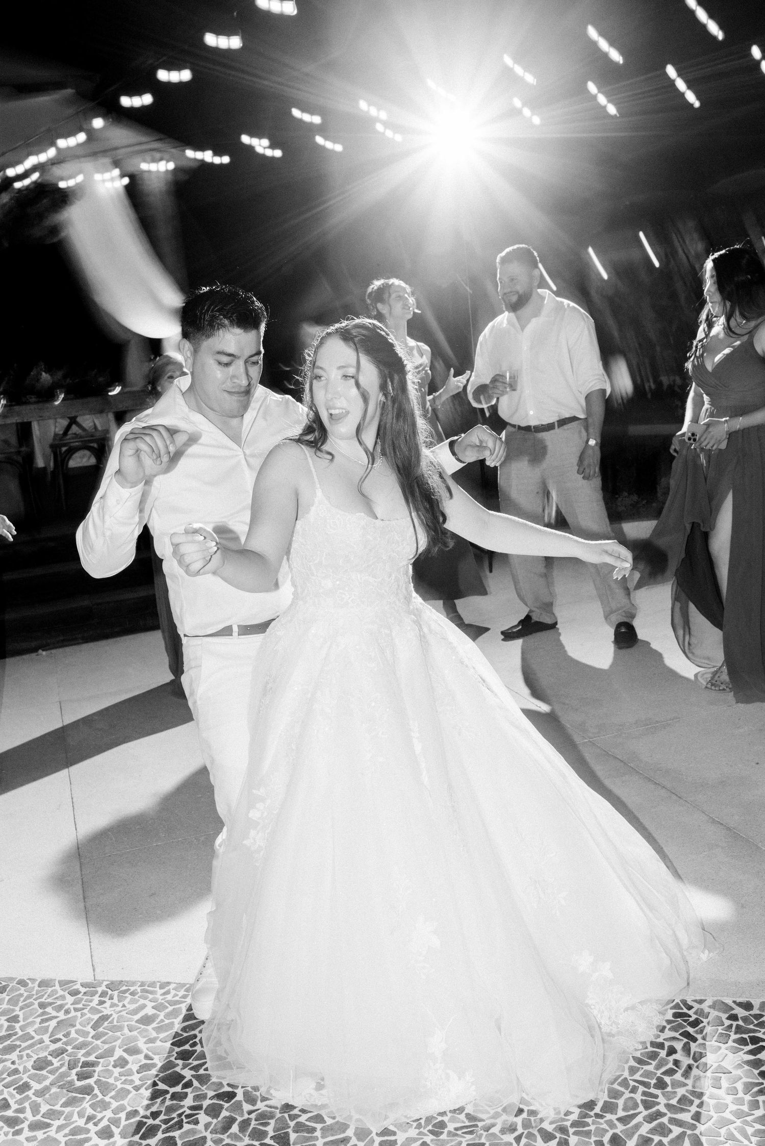 Black and white photo of couple dancing under dramatic lighting at wedding reception.