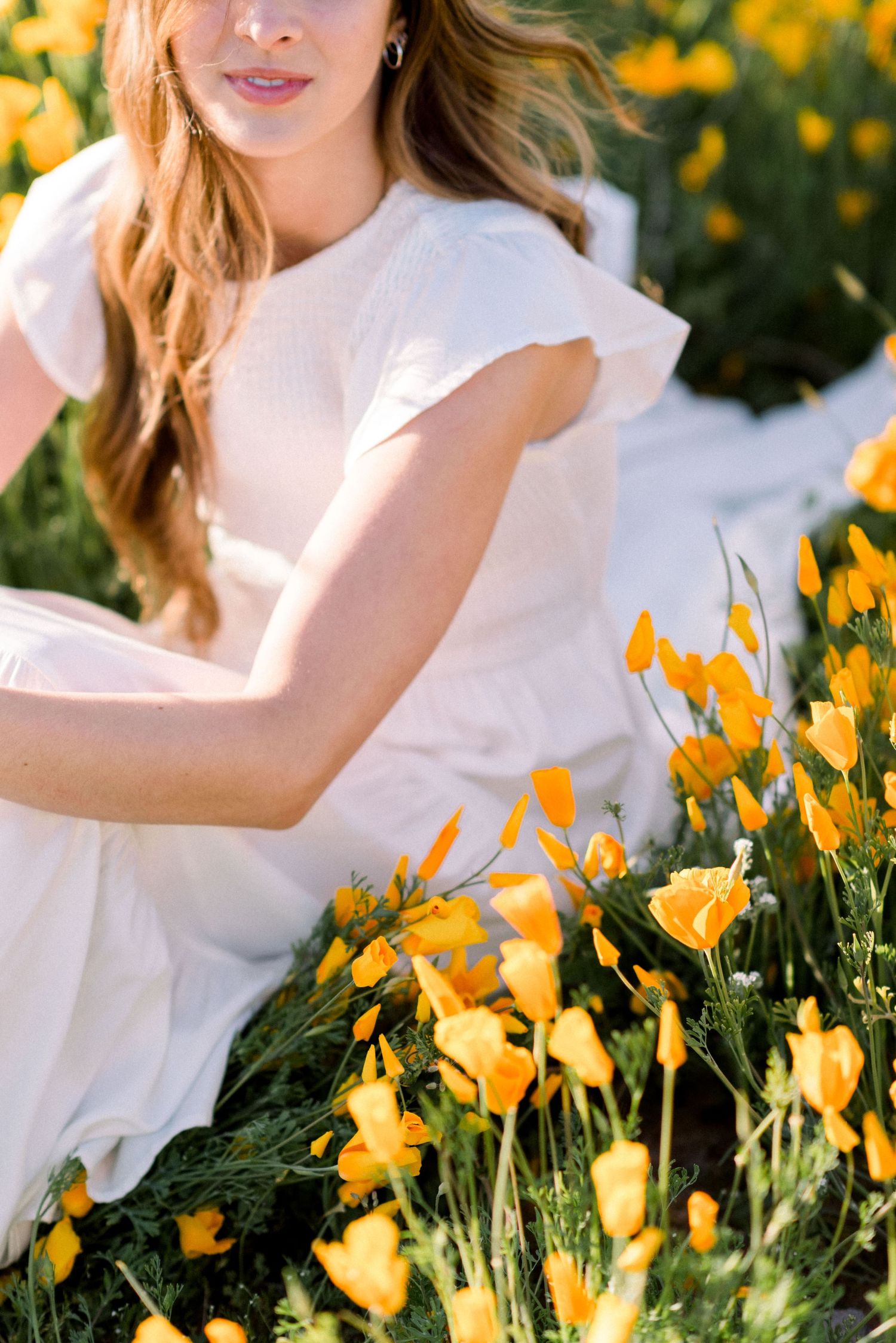 White dress amid blooming yellow poppies creates ethereal spring garden scene.