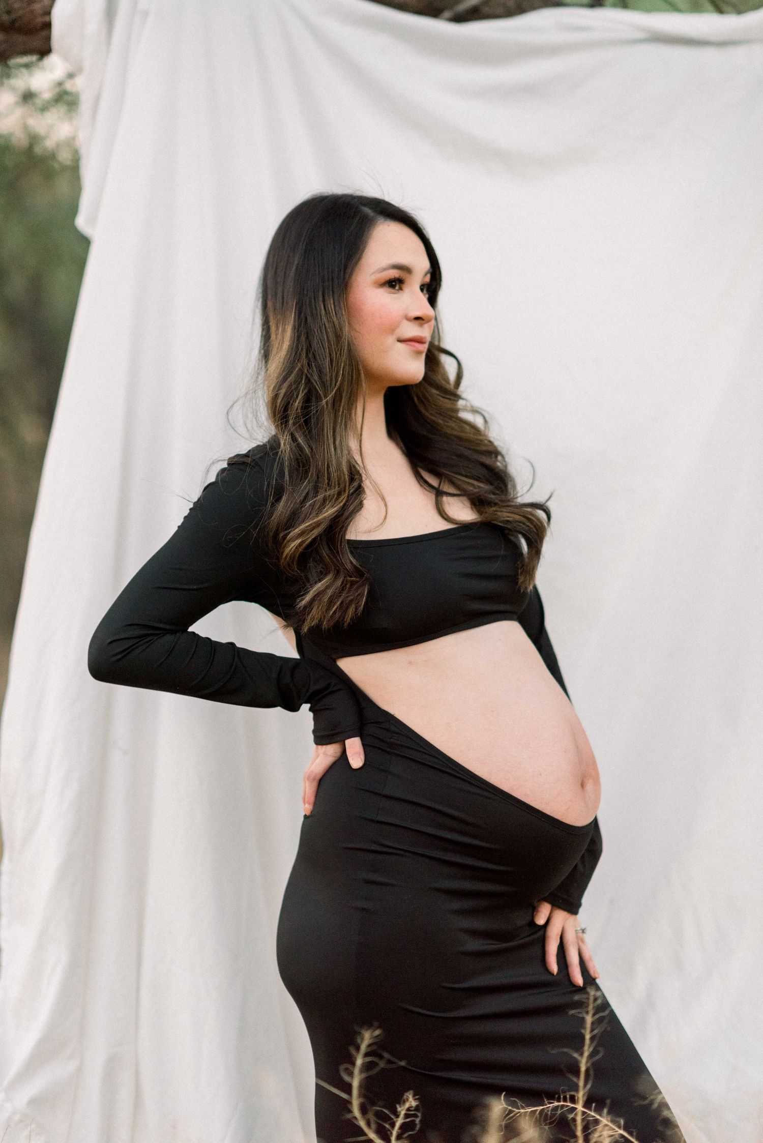 Side view maternity portrait against white backdrop showcasing pregnant belly in black crop top and skirt.