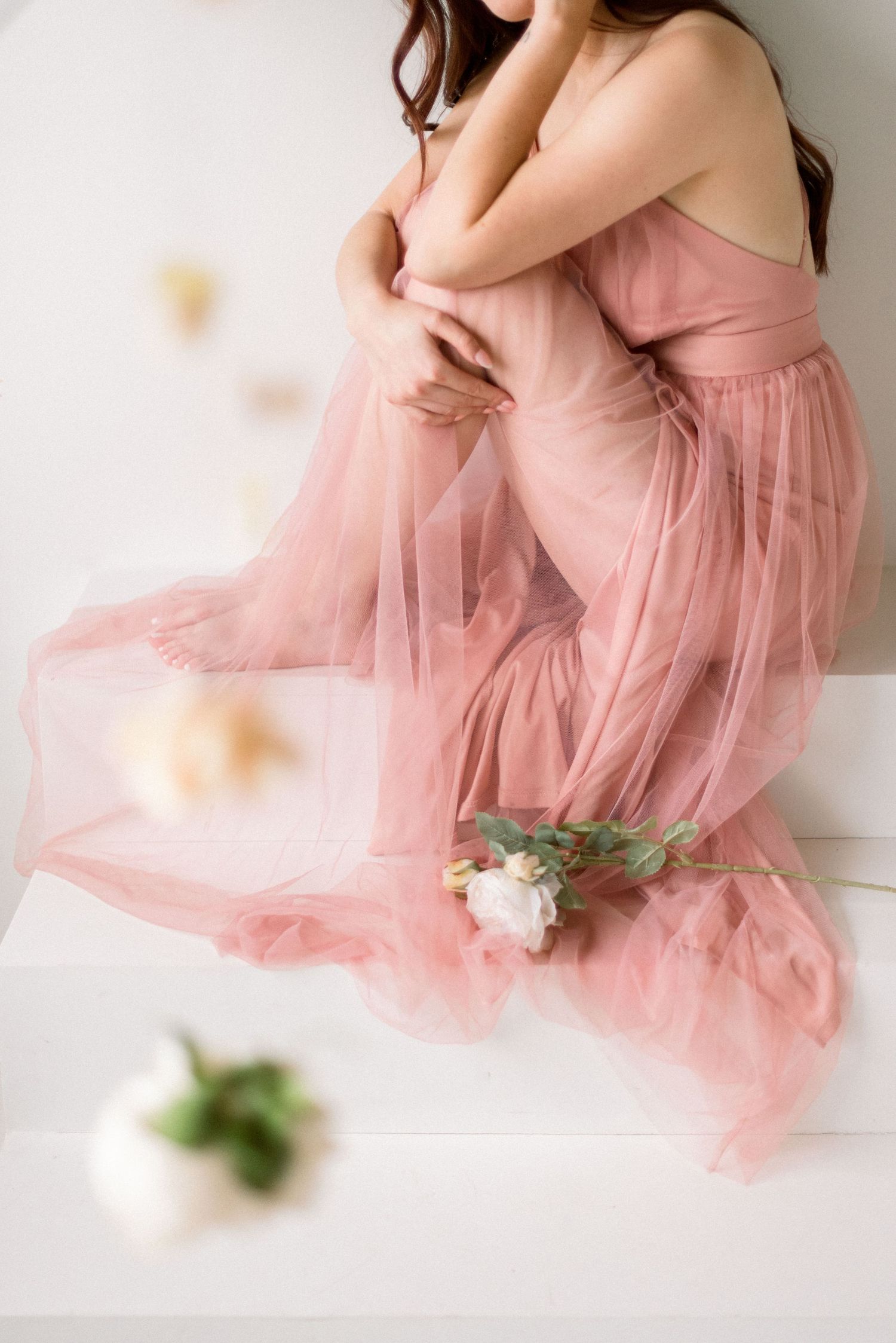 Gentle movement of pink tulle dress captured with floating flowers in minimalist setting.