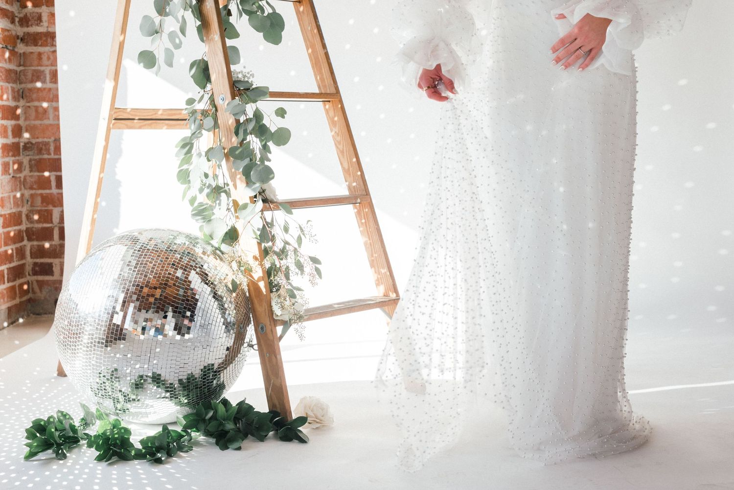 Decorative wooden ladder adorned with greenery and large disco ball on white snowy backdrop.