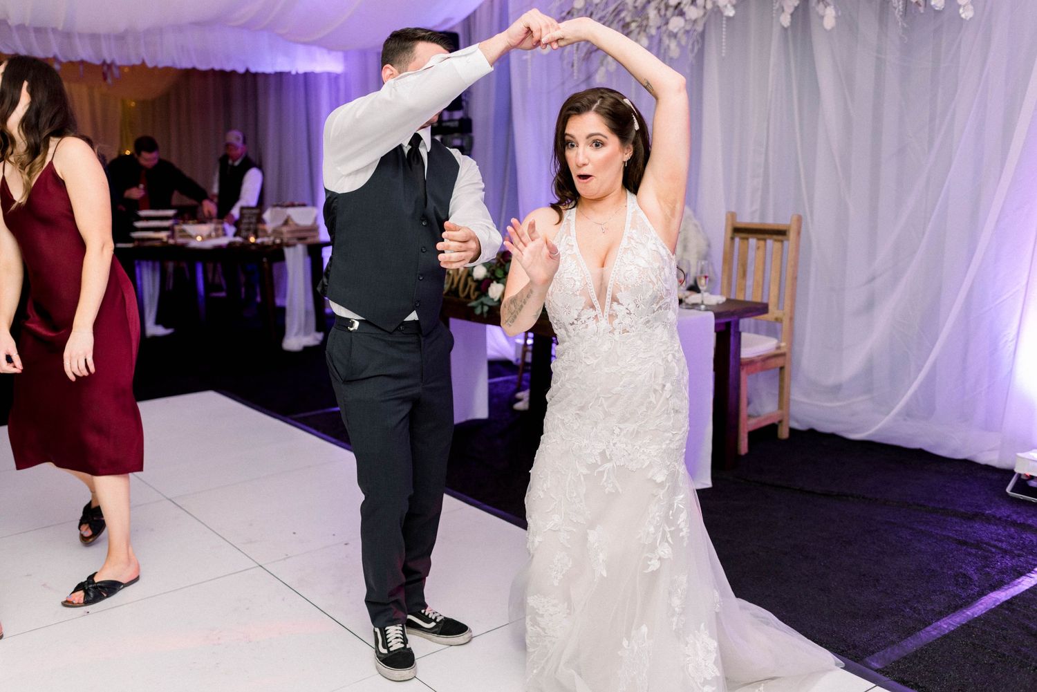 Couple dancing together during wedding reception under draped fabric ceiling with purple lighting.