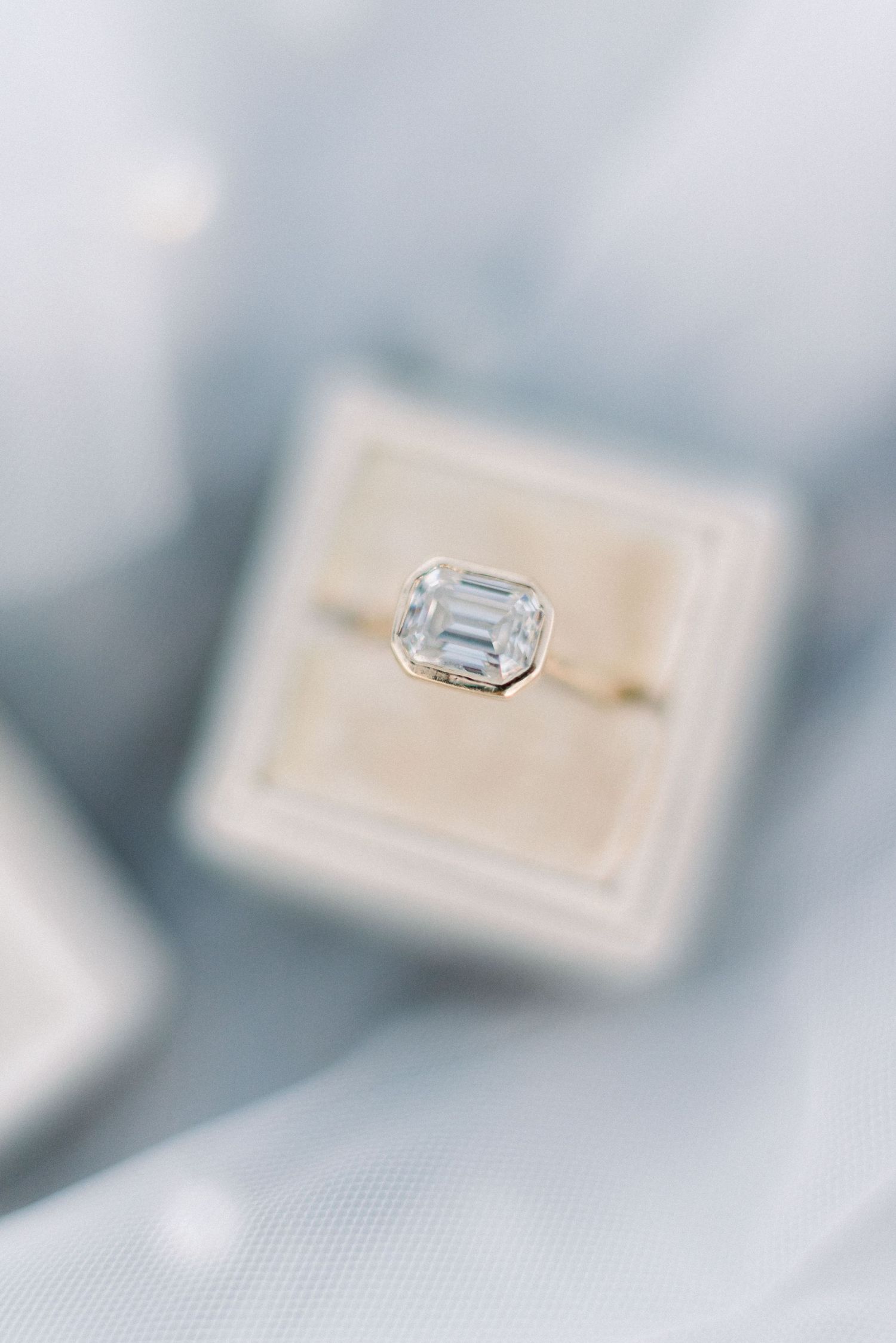 Emerald cut diamond engagement ring in a beige ring box with soft focus.