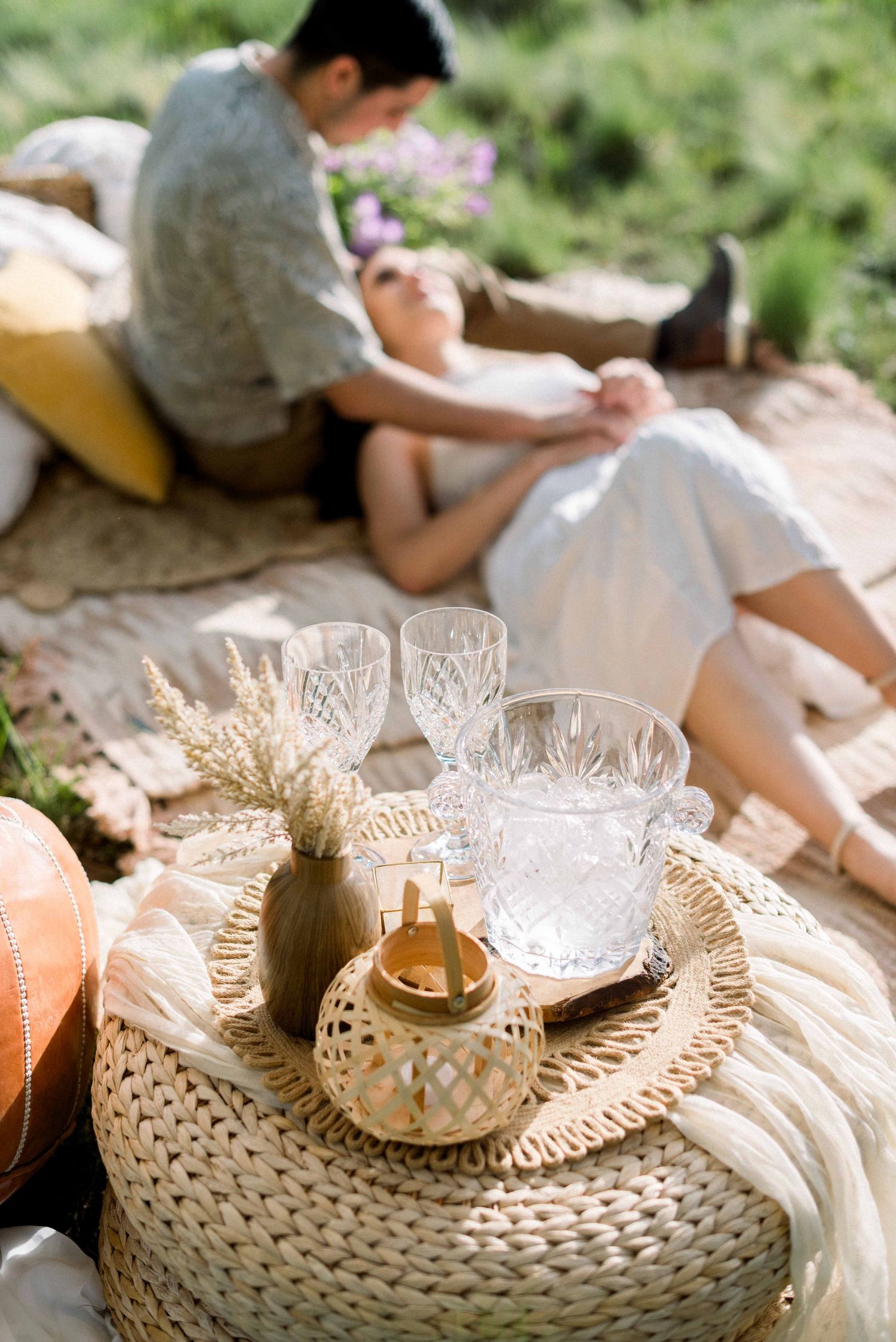 Crystal glasses and decorative elements on woven tray during romantic outdoor picnic.