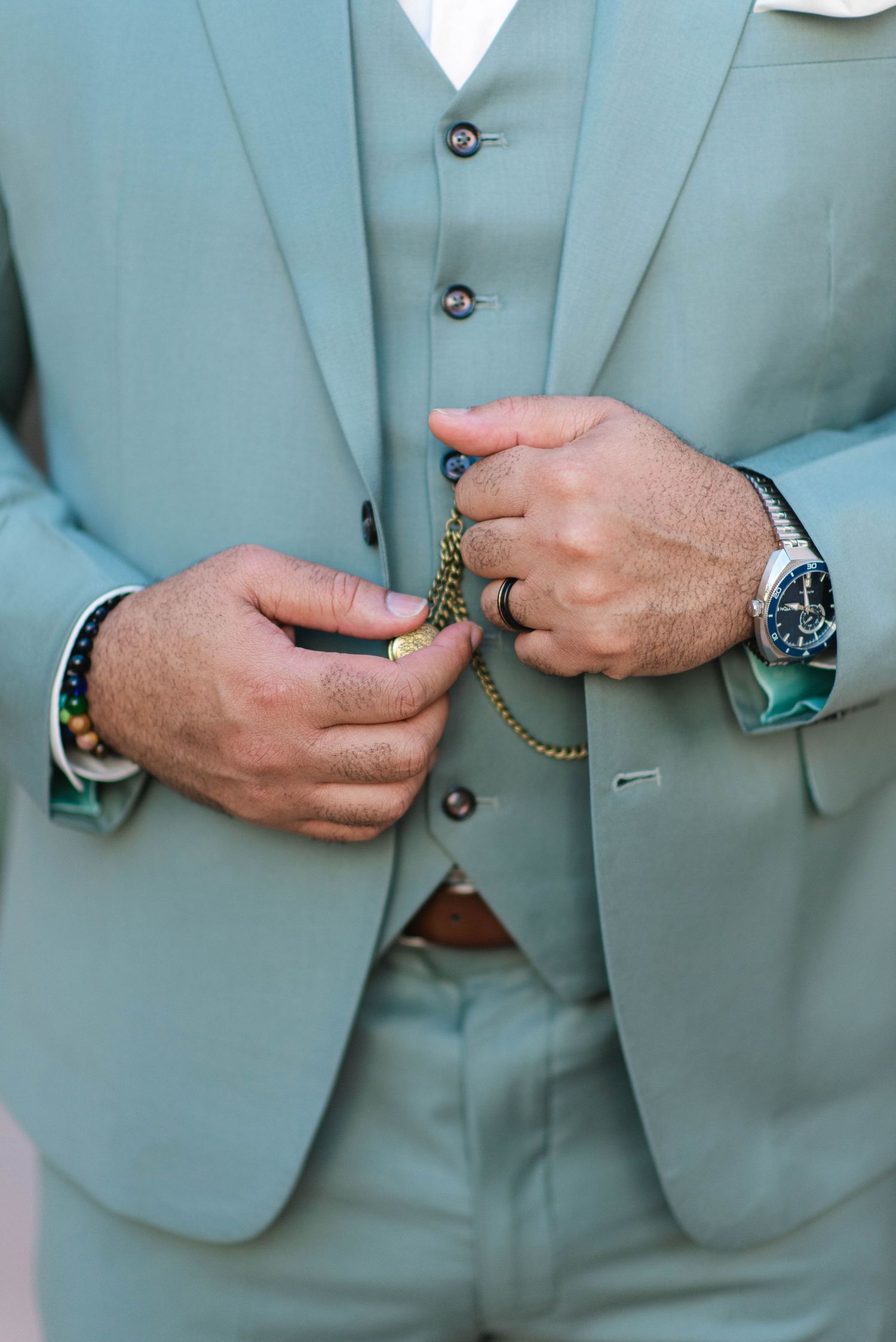 Close-up of hands adjusting a pocket watch chain on a mint green three-piece suit.