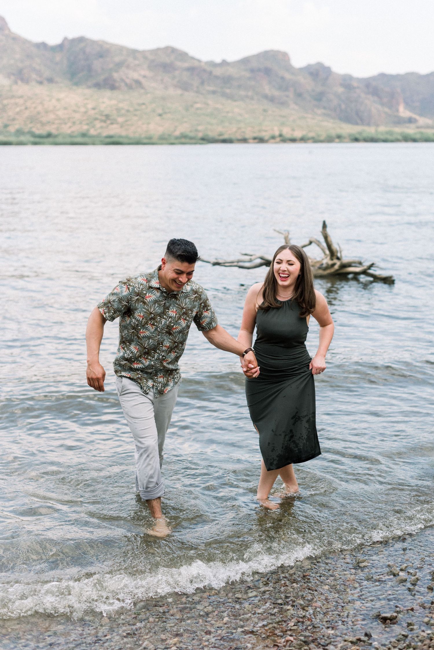 A couple splashes and plays together in the shallow waters of a lake with mountains in the background.