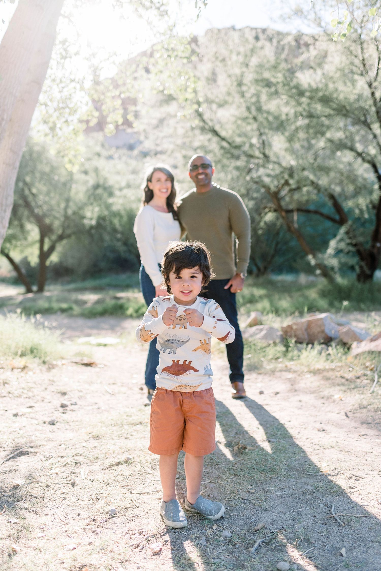 A family enjoying a playful moment together in an olive grove on a sunny afternoon.