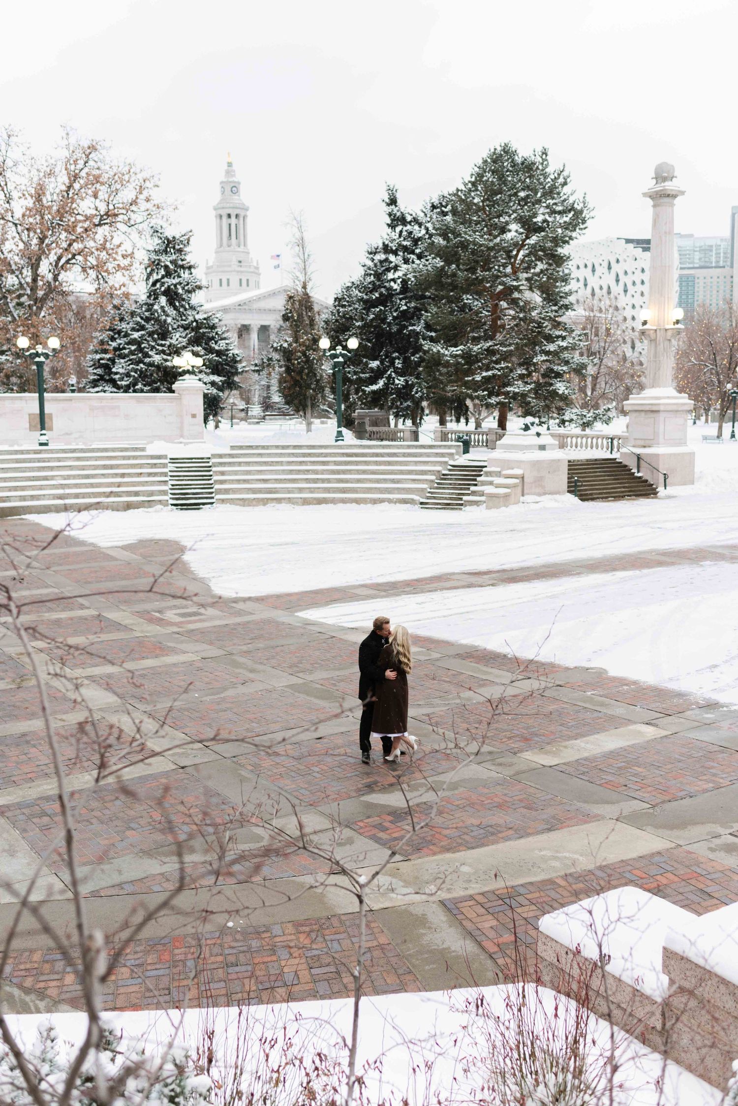 A distant view of two people walking in a snow-covered plaza with a church spire in the background.