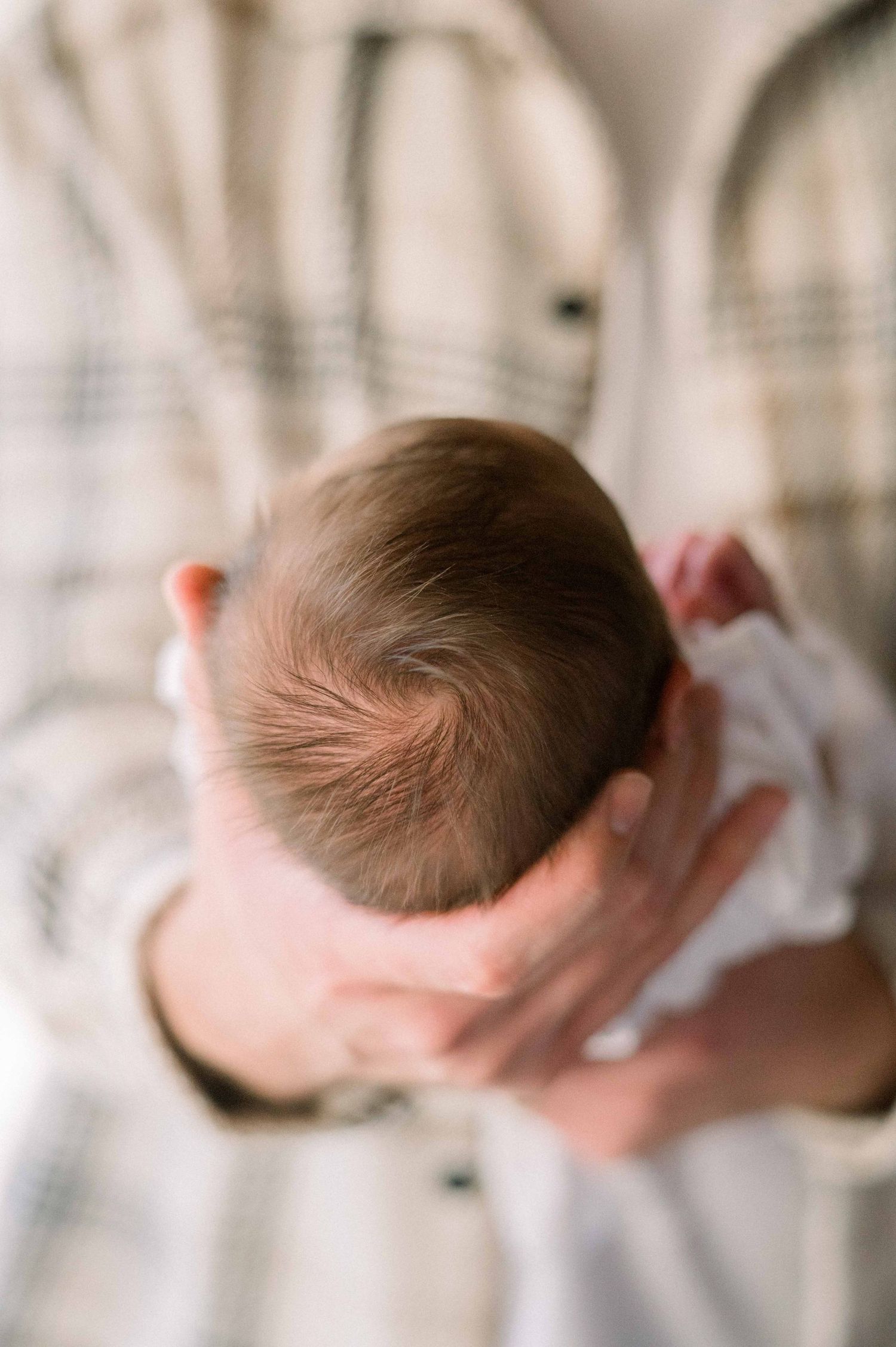 Top view of newborn's head showing soft hair while being held in plaid-shirted arms.