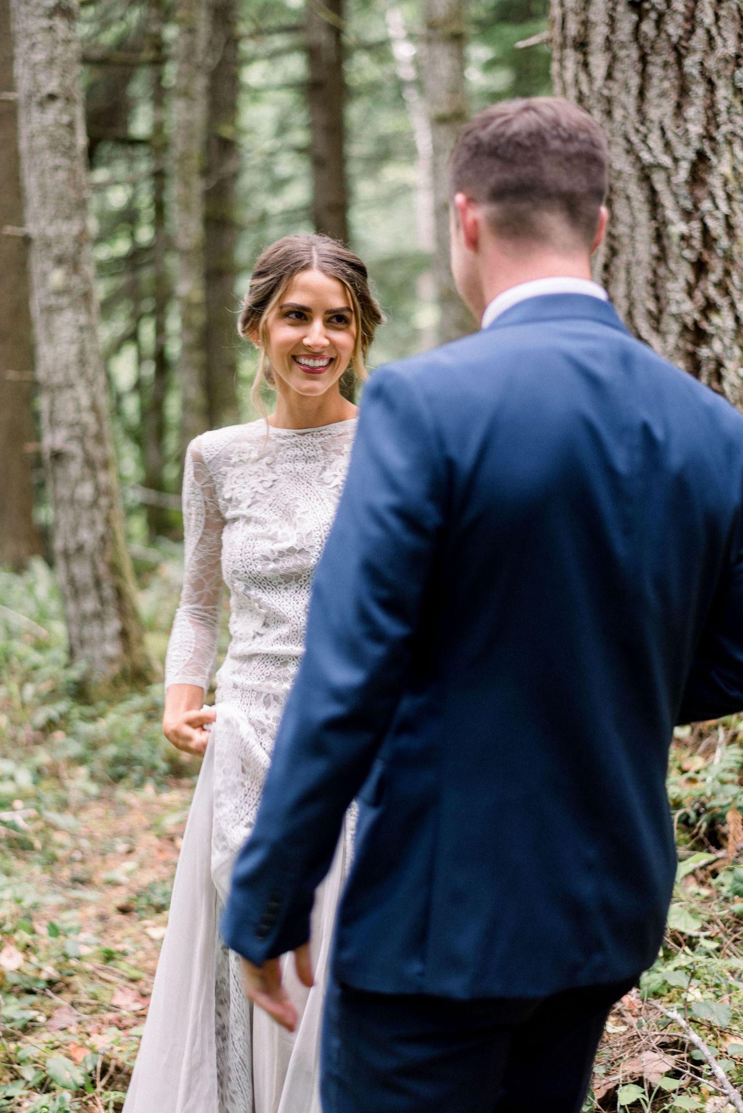 A first look moment between newlyweds in a forest setting with the bride wearing a lace gown.