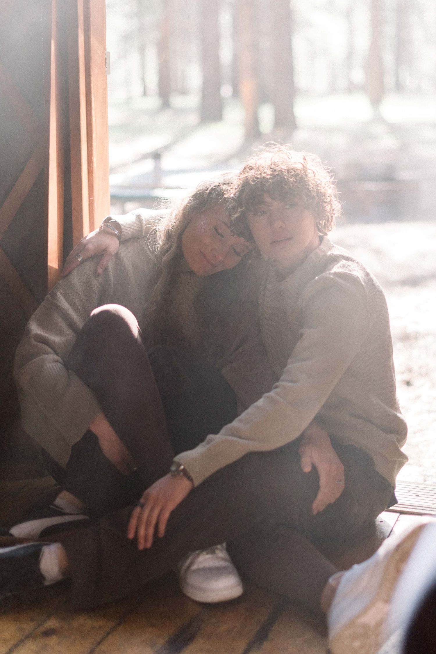 Two people in matching sweaters sharing intimate moment near window.