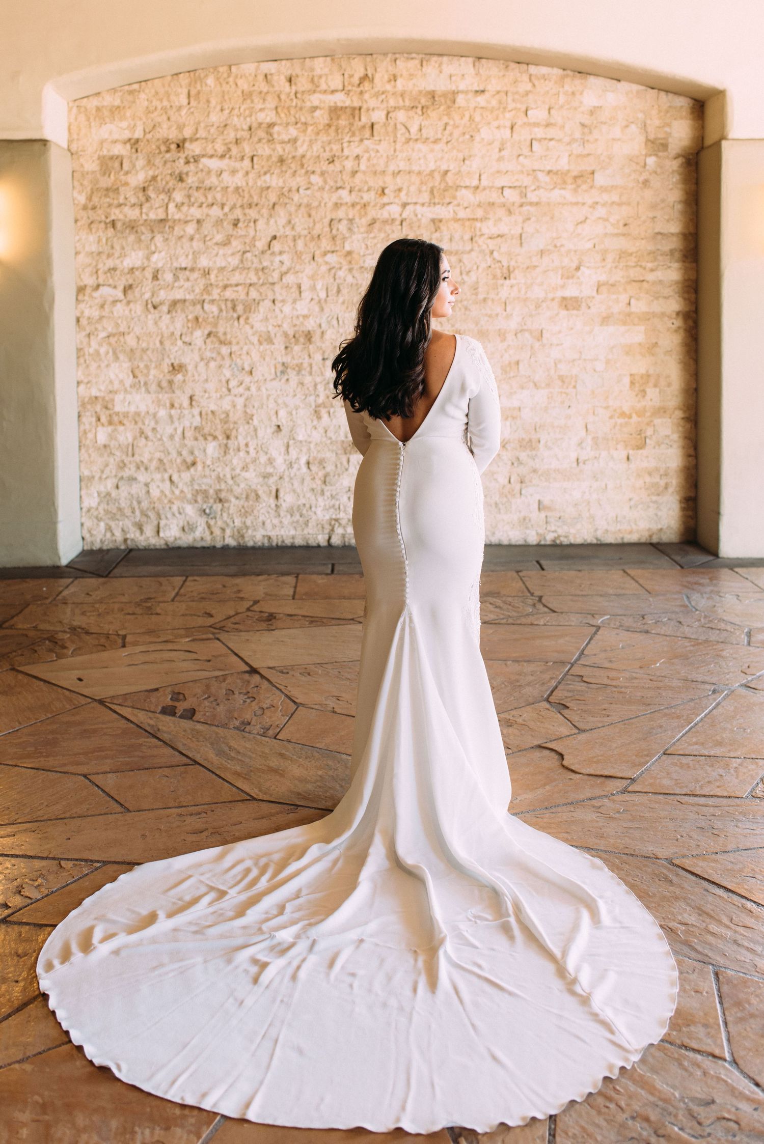 Elegant white wedding dress with dramatic long train shown against stone archway backdrop.