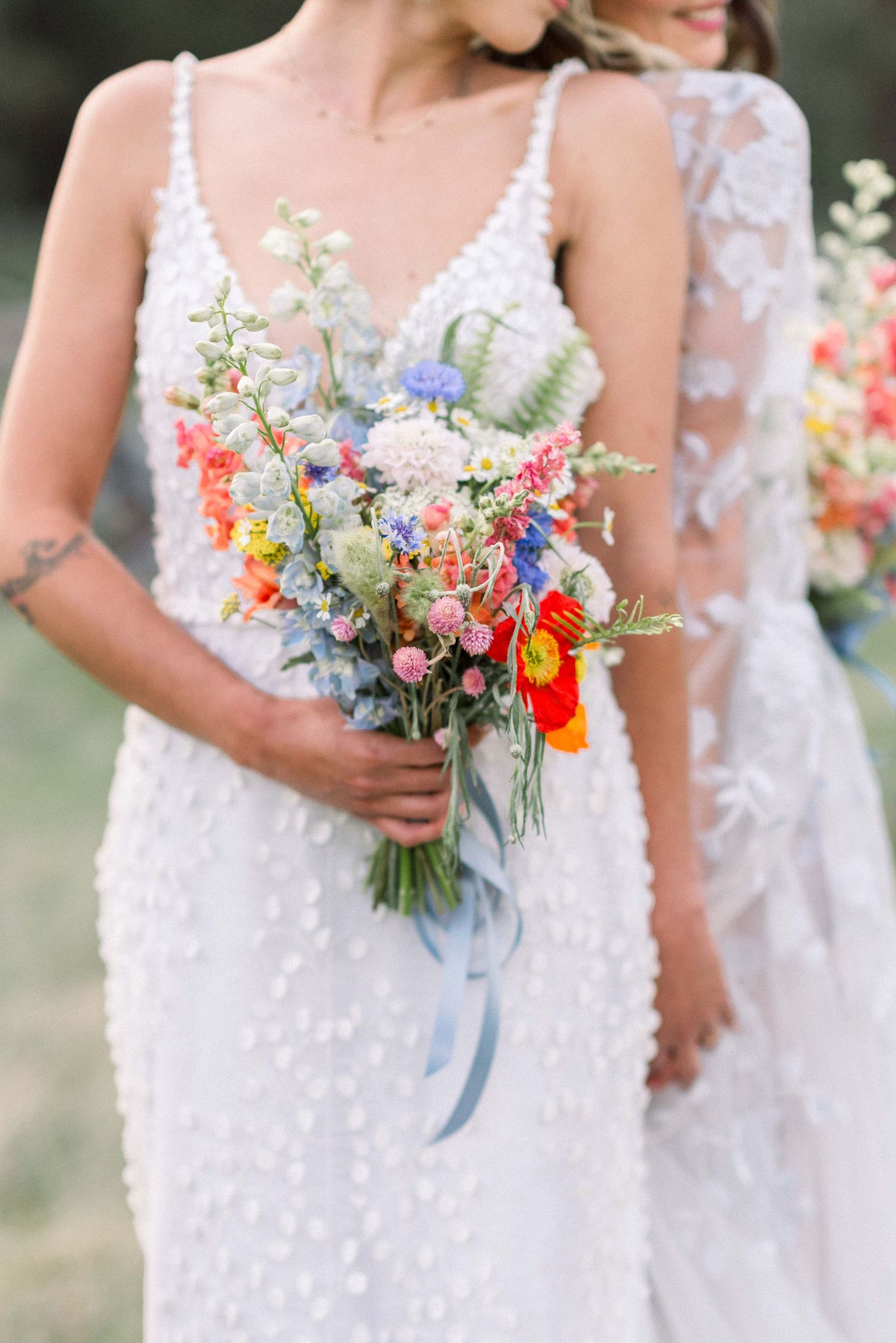 Close-up of a wildflower bouquet with orange poppies and blue ribbons against a white lace wedding dress.