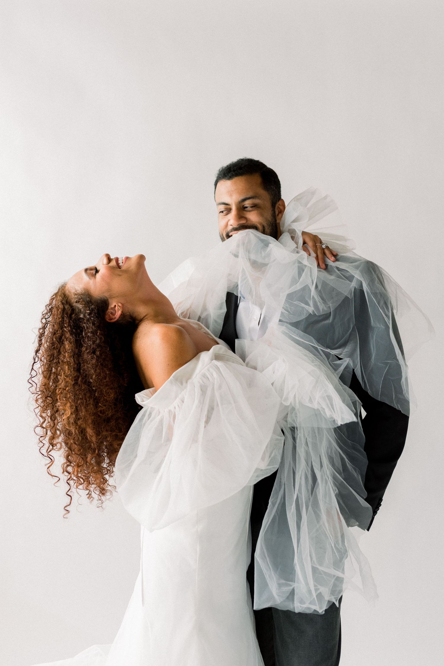 Contemporary wedding photo with couple embracing and laughing in white and black formal wear.