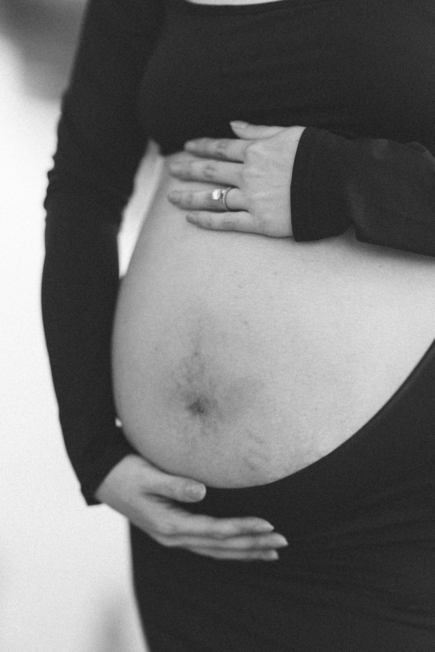 Close-up black and white photo of pregnant belly with hands framing the bump.