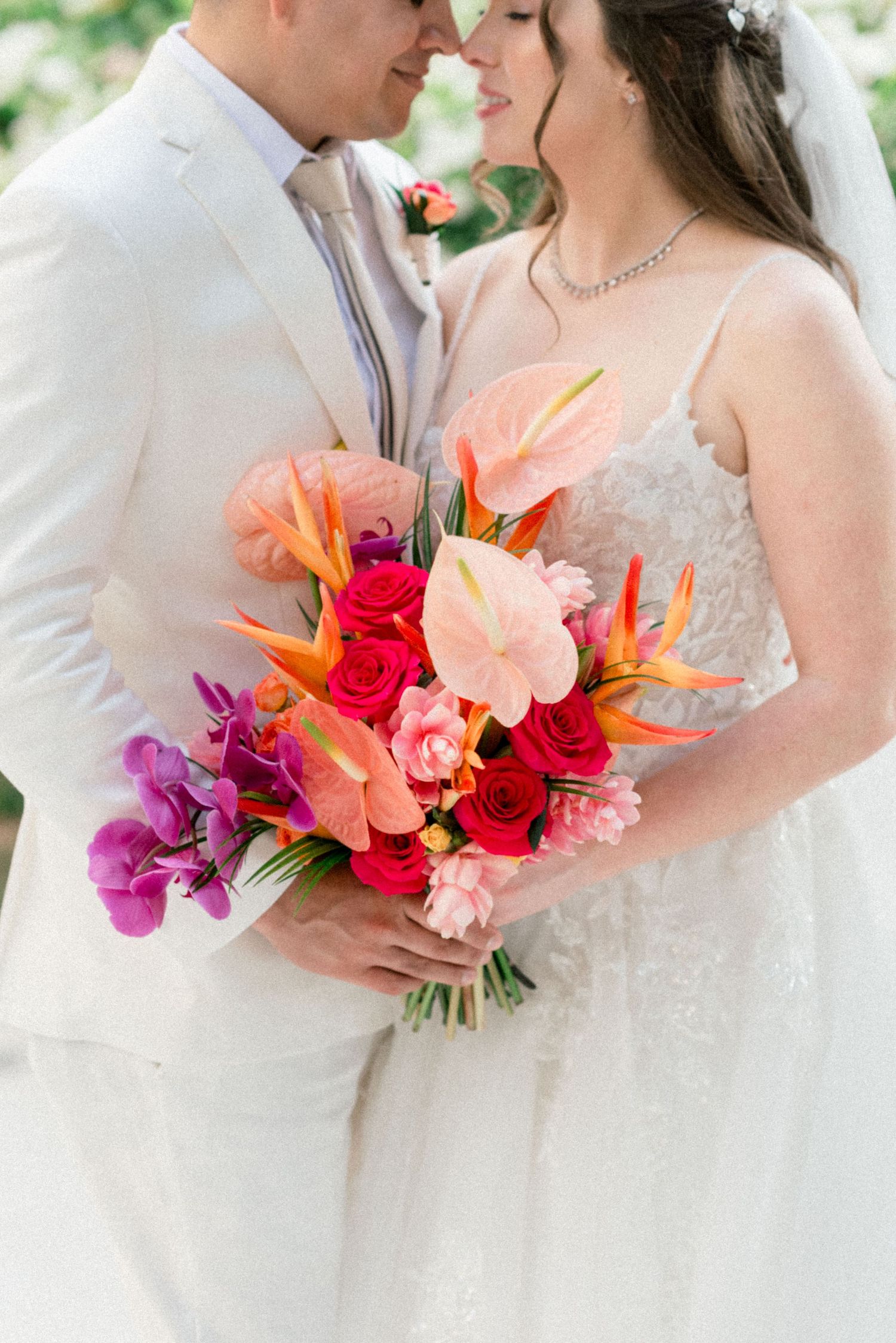 Close-up of wedding couple sharing intimate moment with colorful tropical bouquet.