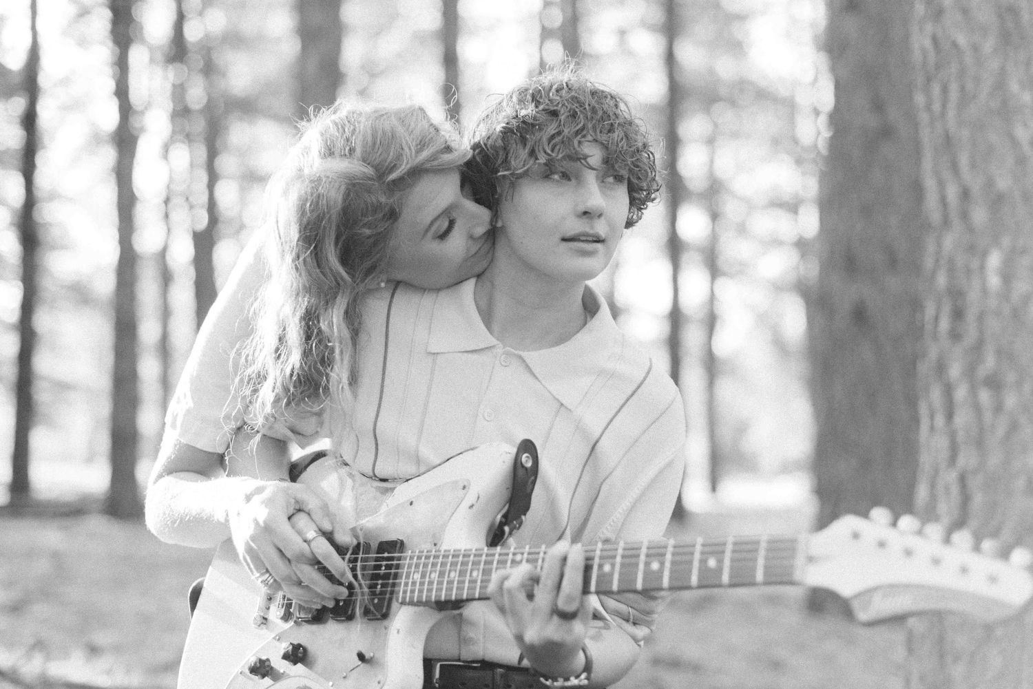Black and white portrait of couple sharing tender moment with guitar outdoors.