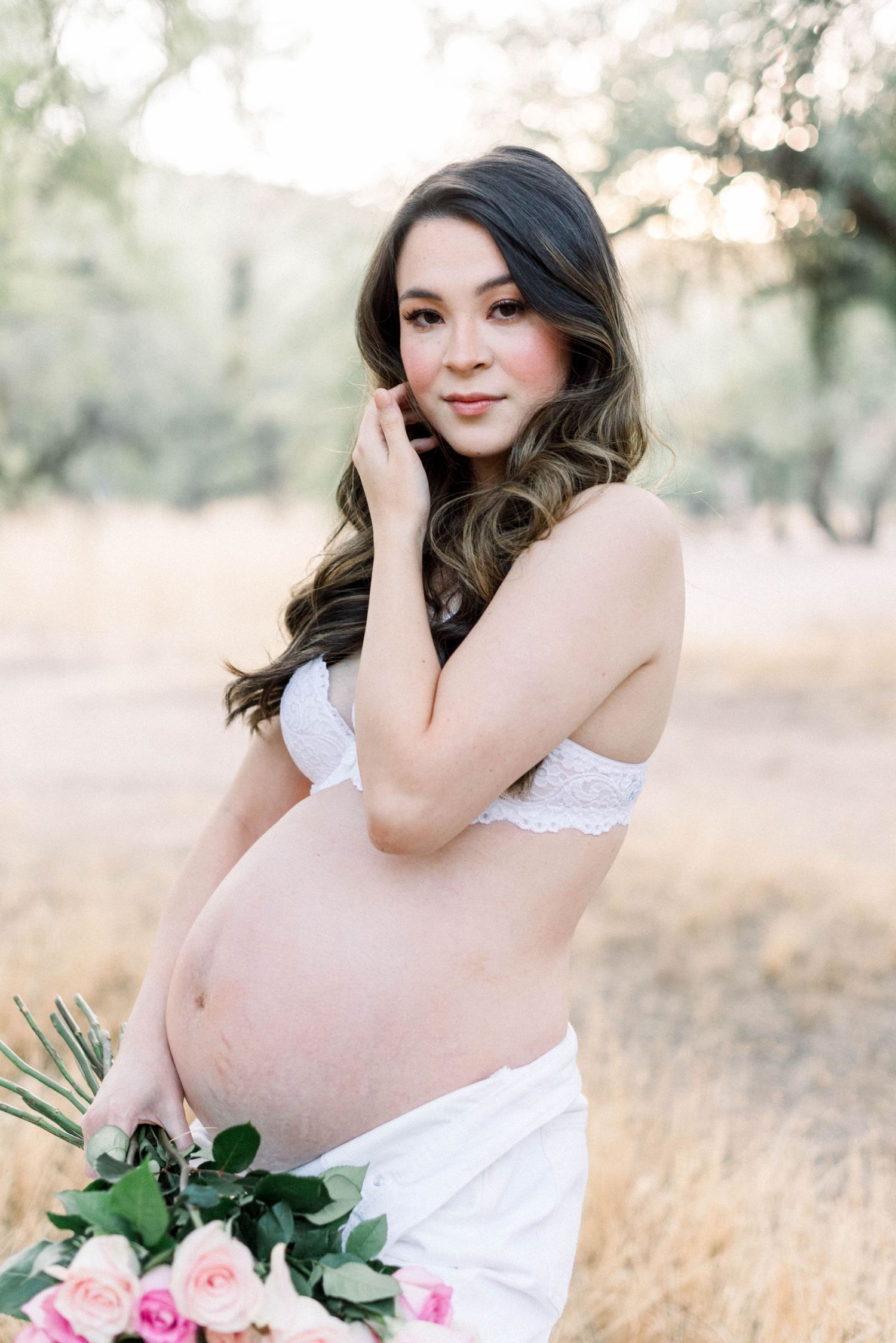 Maternity photoshoot in a field with white fabric and pink roses during golden hour.