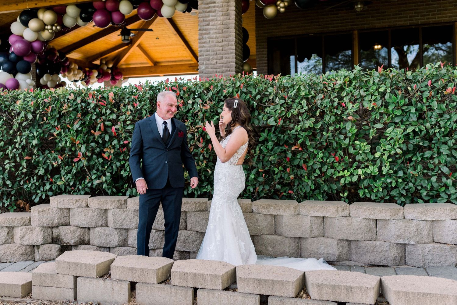 A couple shares their wedding first look on stone steps surrounded by greenery and balloon decorations.