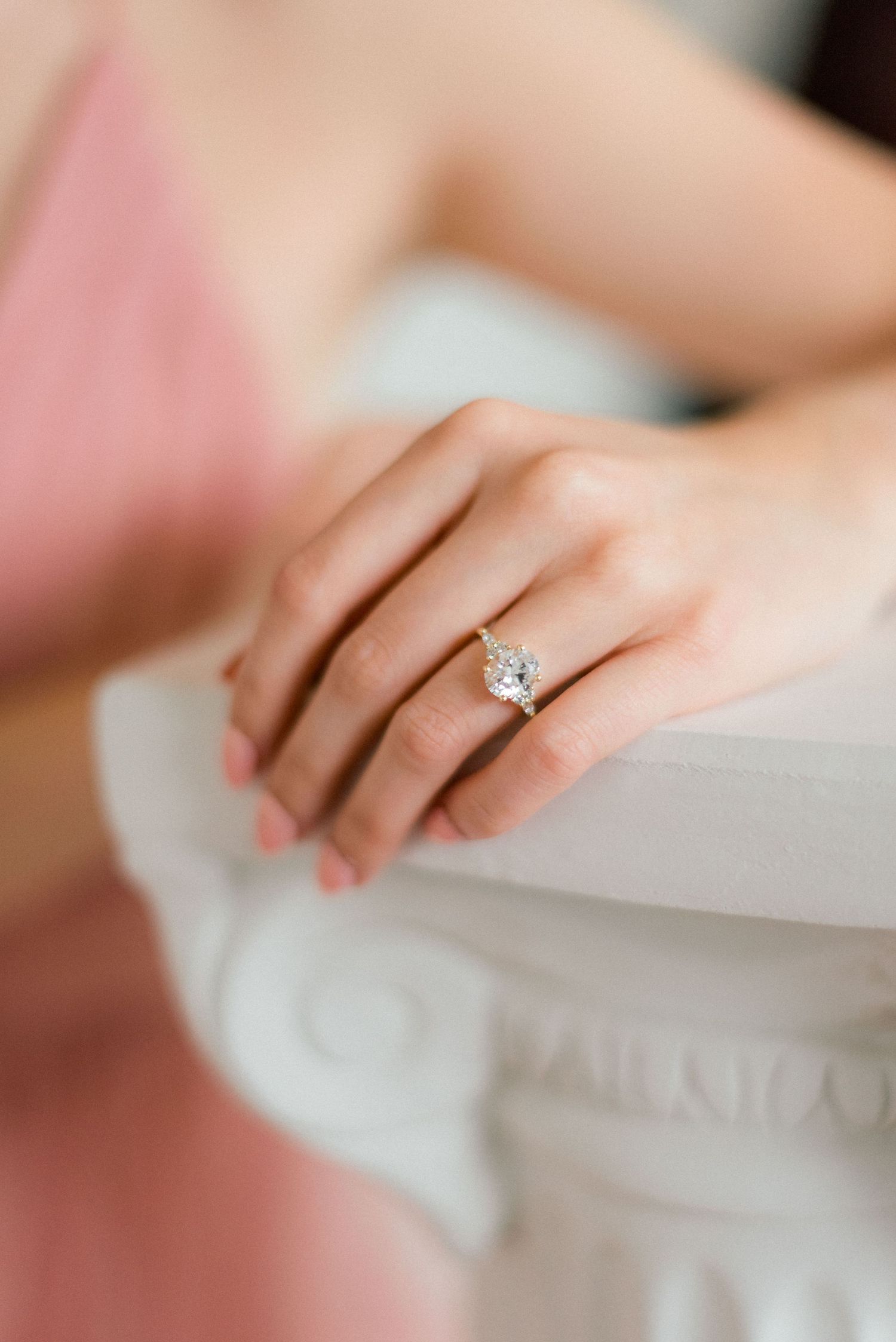 Elegant solitaire diamond engagement ring showcased on hand against white surface.