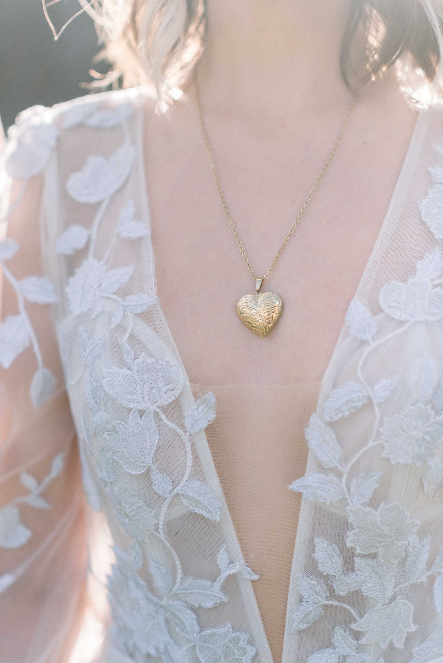 Delicate gold heart necklace worn with white lace wedding dress detail.