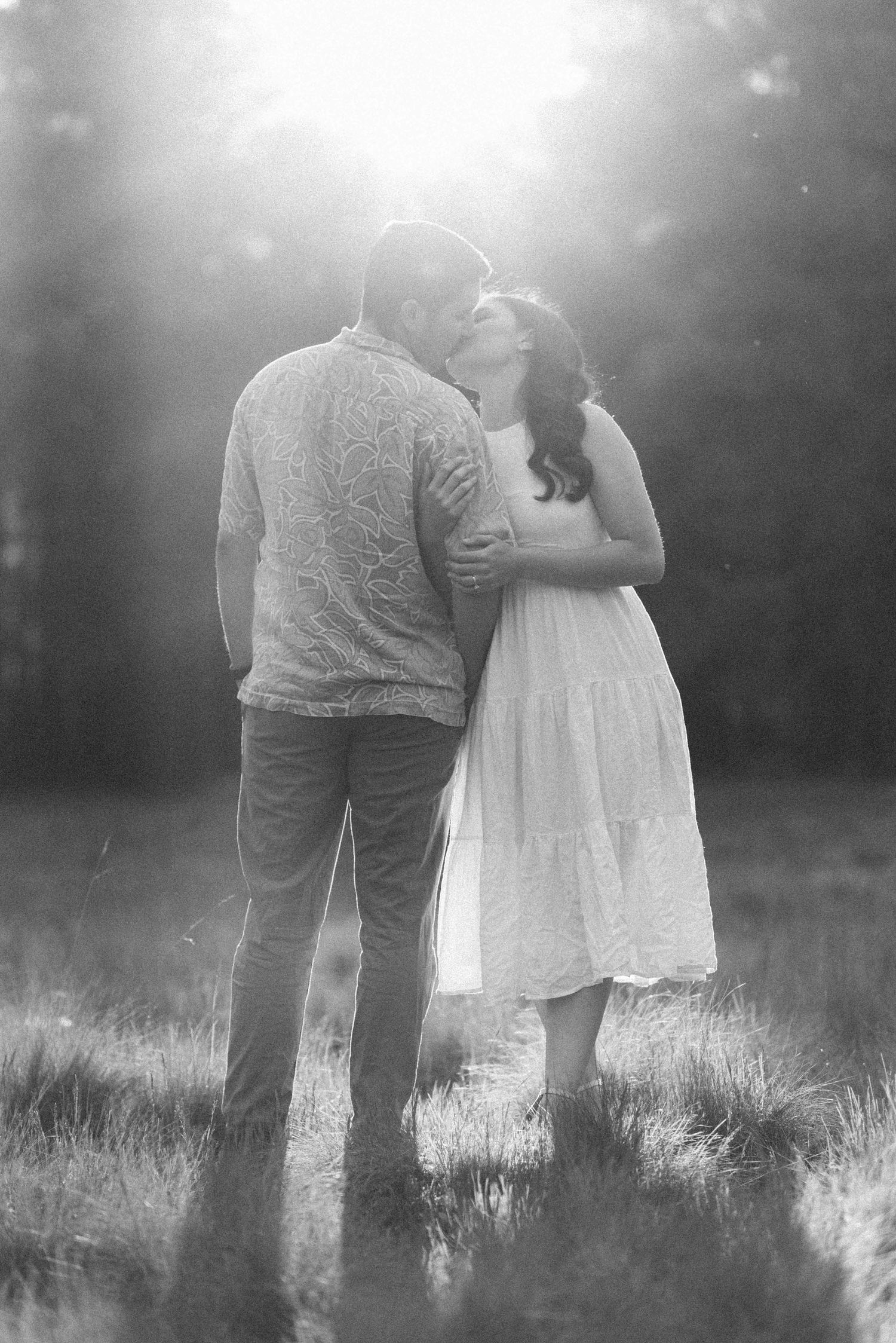 Black and white portrait of a couple embracing in a misty meadow at sunset.