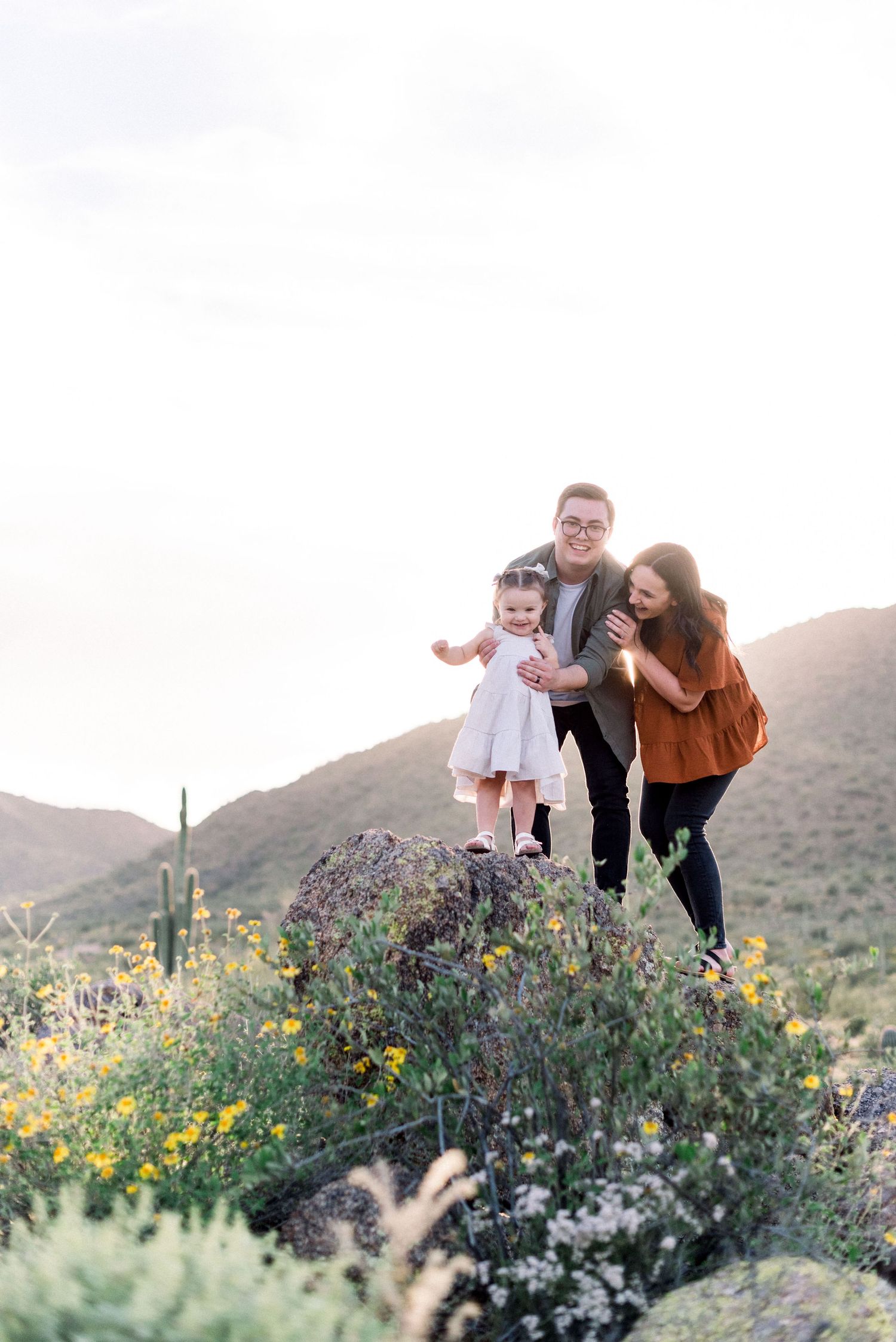 Family enjoying time together among desert wildflowers with mountains in background.