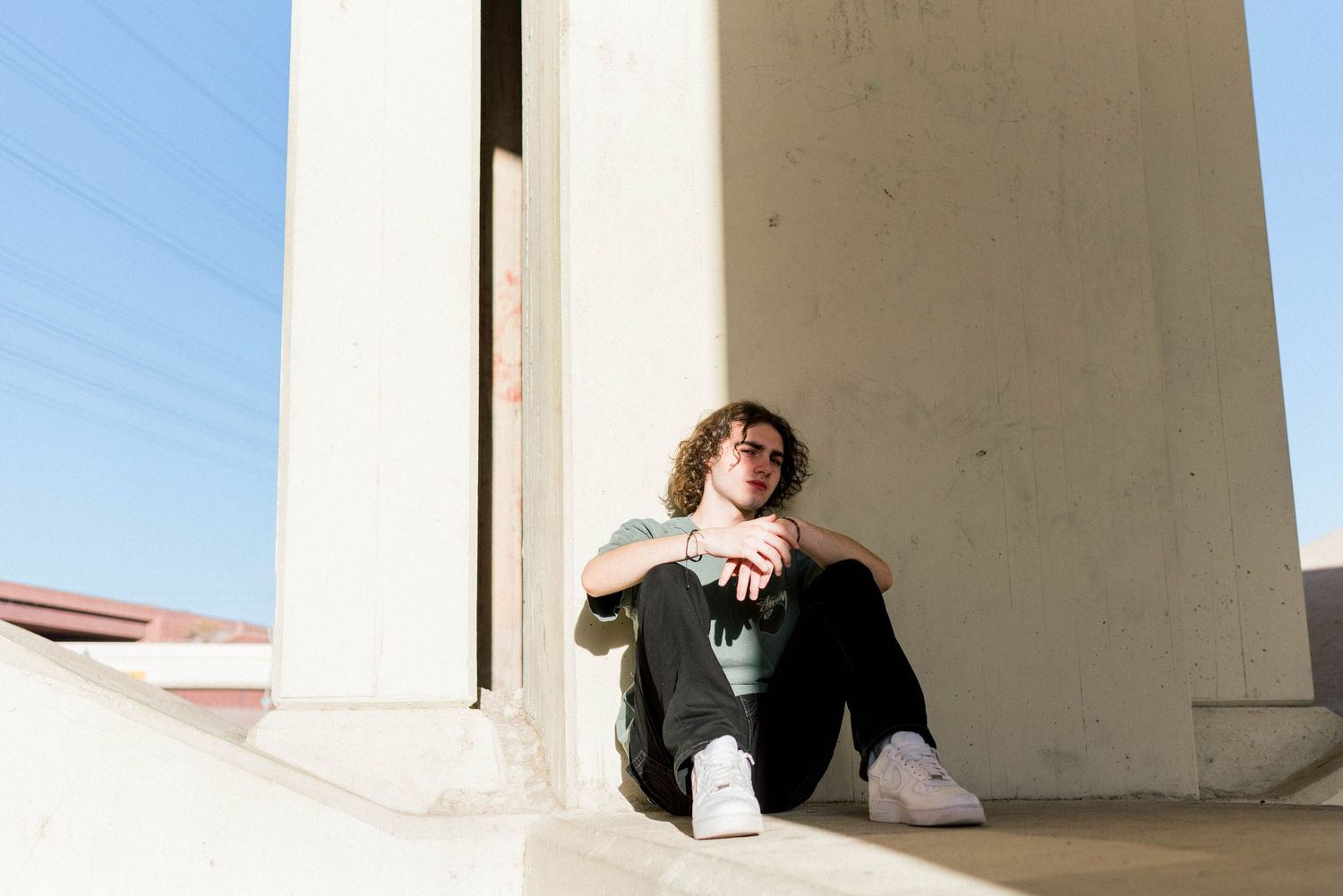 Person relaxing in urban setting against concrete pillar with blue sky background.