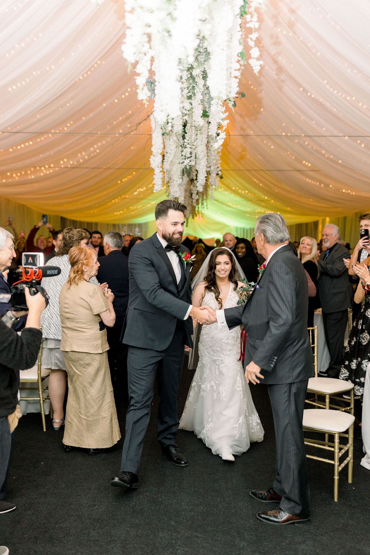Wedding celebration in elegantly draped reception venue with guests capturing the moment on phones.