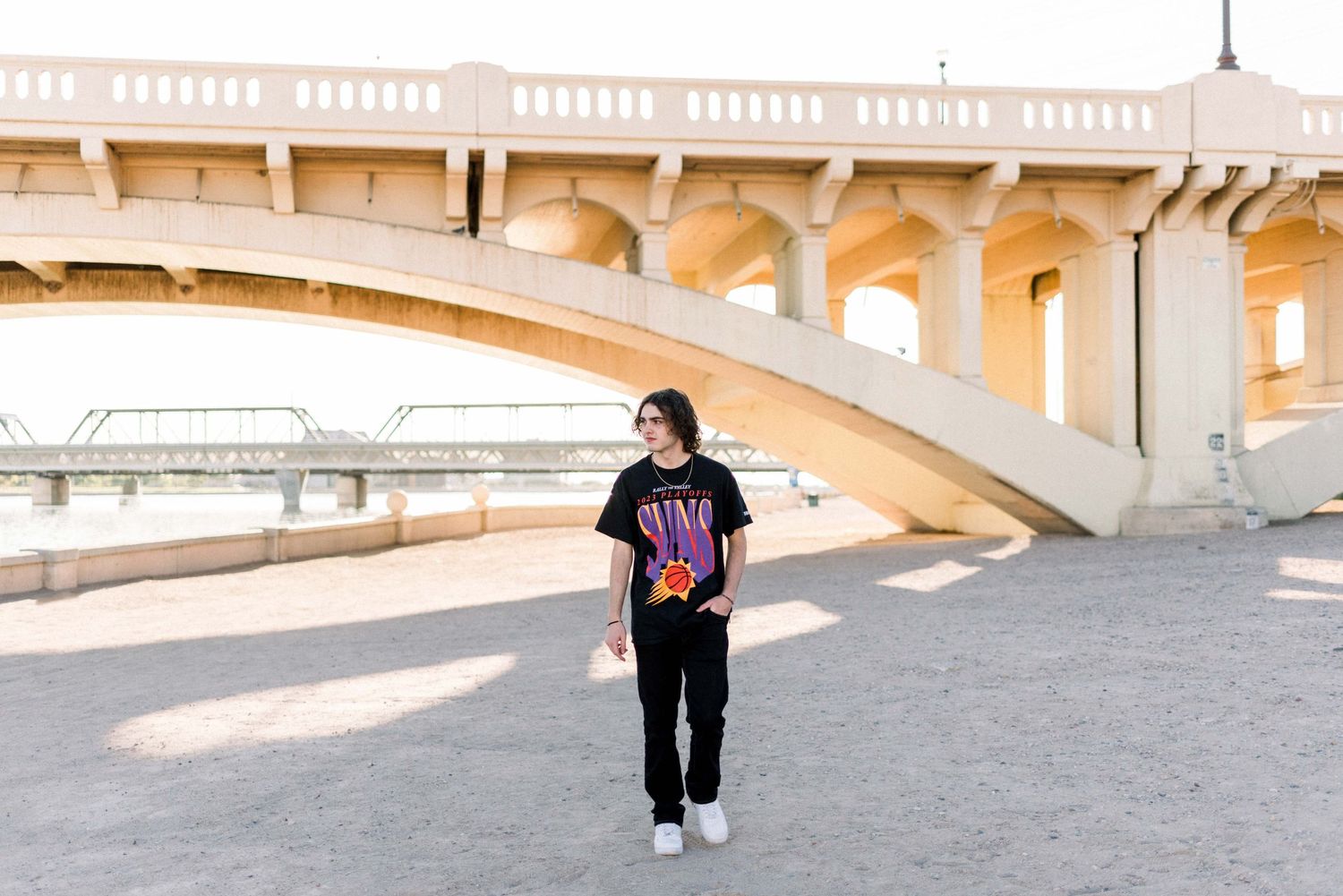 Person in black t-shirt standing under concrete bridge structure.
