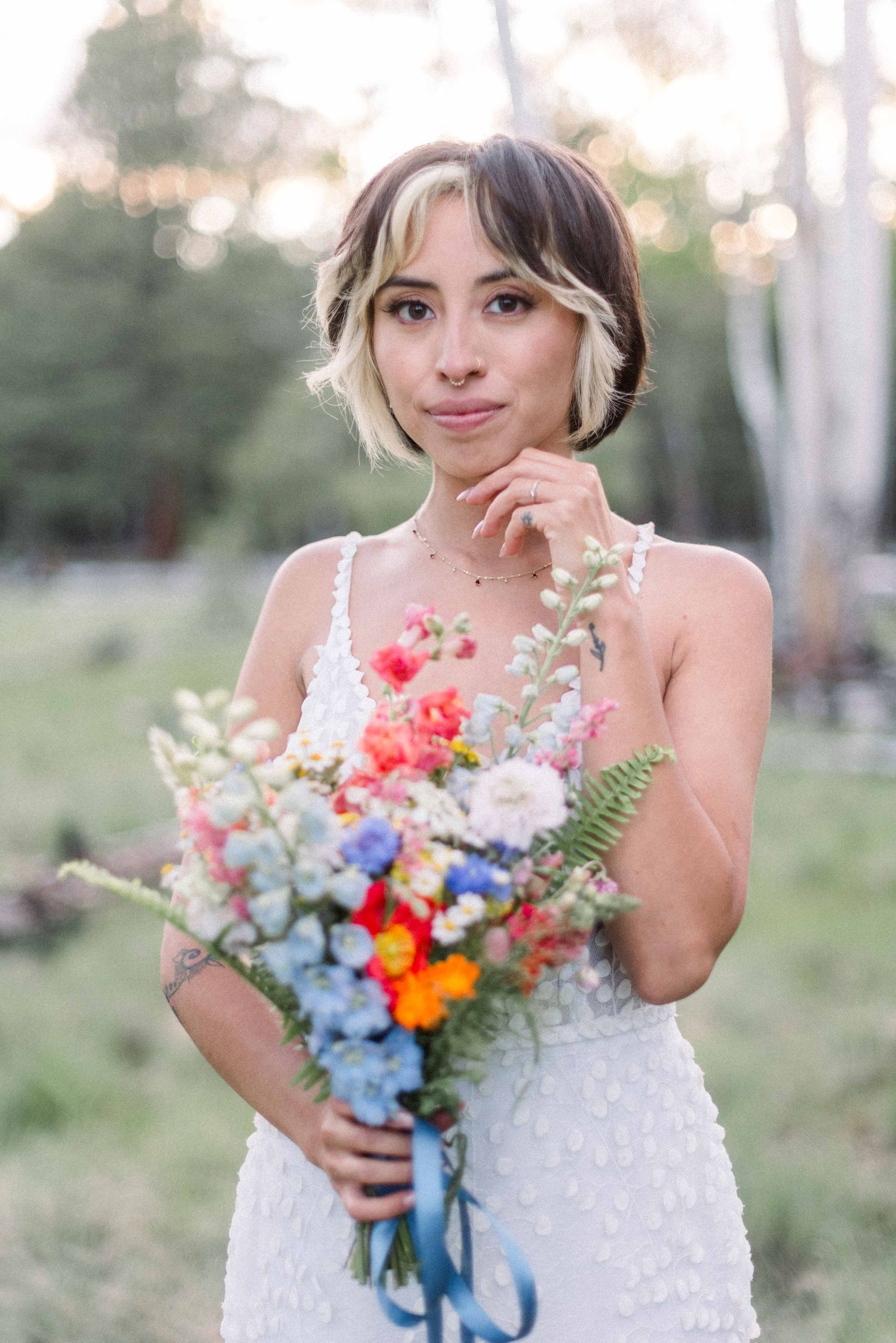 Person in white lace dress holding vibrant wildflower bouquet with delicate floral details.