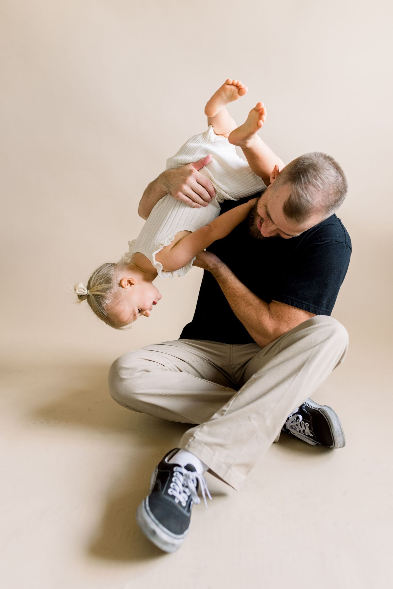 A playful scene of a parent holding a toddler upside down against a neutral backdrop.