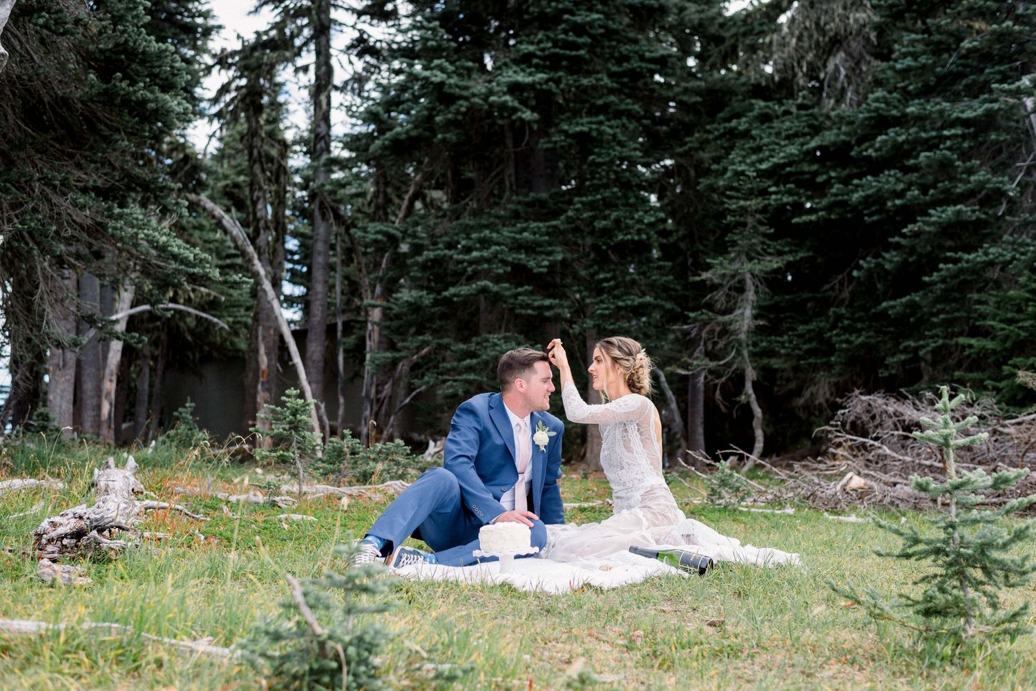 Couple shares an intimate moment on a blanket in an alpine forest clearing.