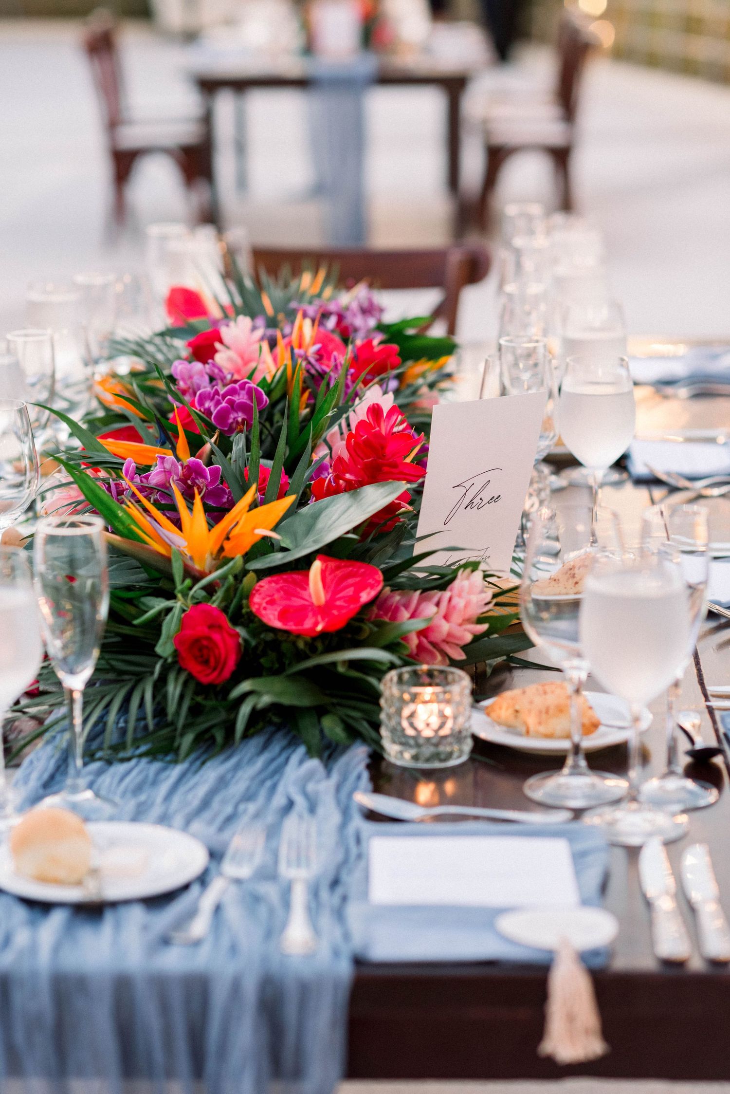 Vibrant tropical floral centerpiece with bright pink and orange blooms on a wedding reception table.